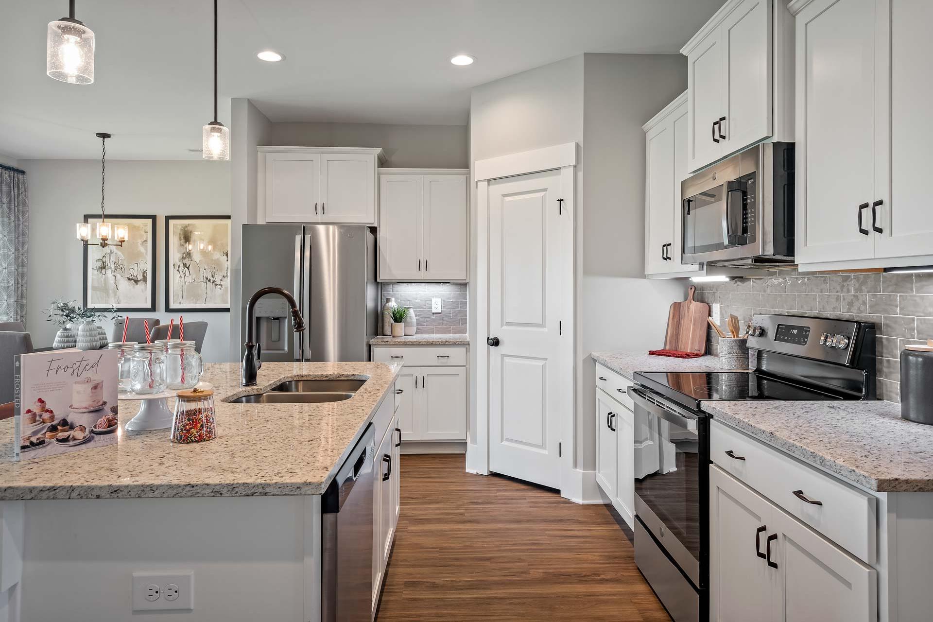 Spacious modern kitchen at Heritage Lakes in New Market AL with white cabinets, granite island, stainless steel appliances, and hardwood floors