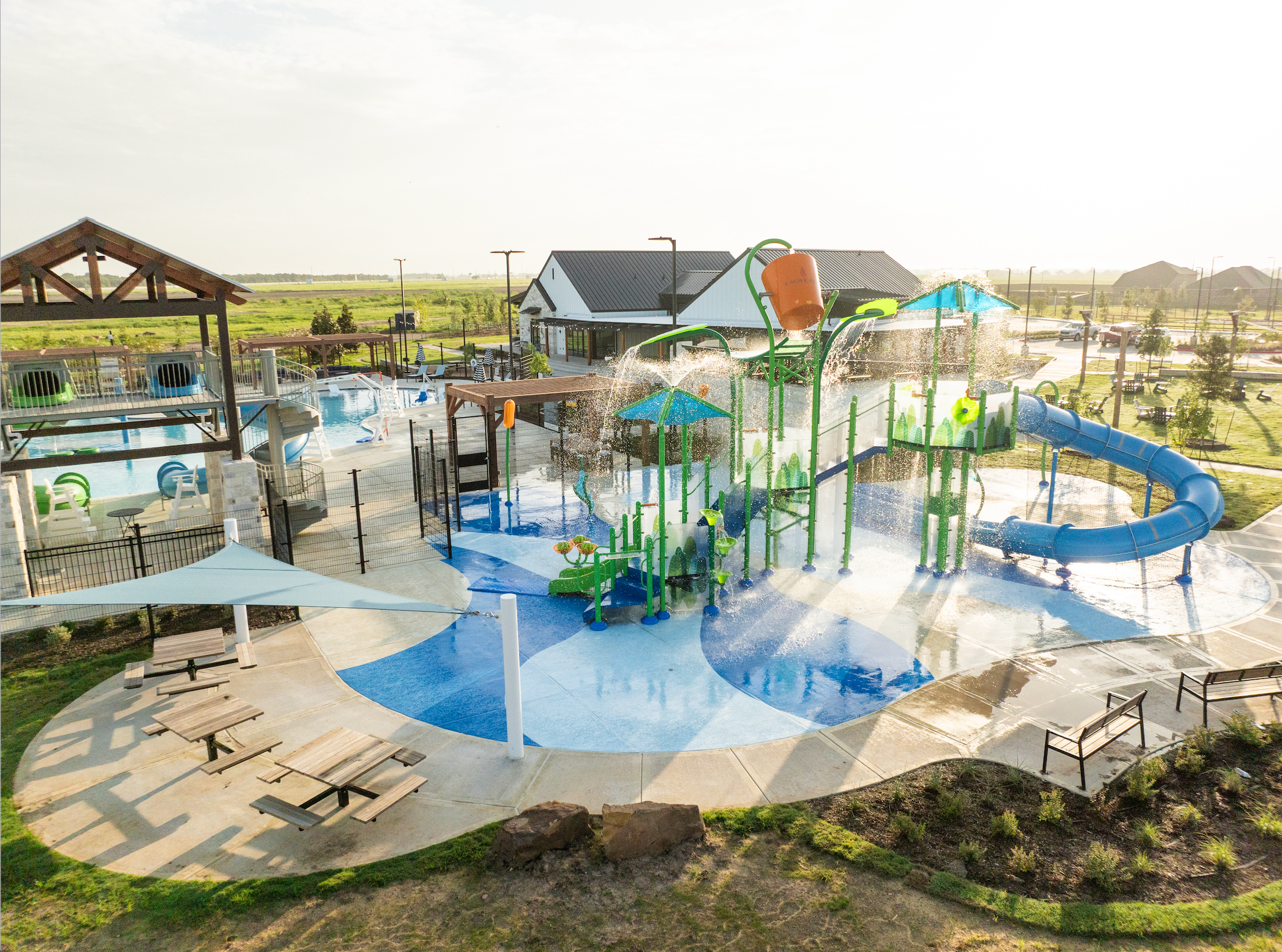 Vibrant splash pad at Emberly in Beasley Texas with green water towers blue slides spraying fountains and lounge seating