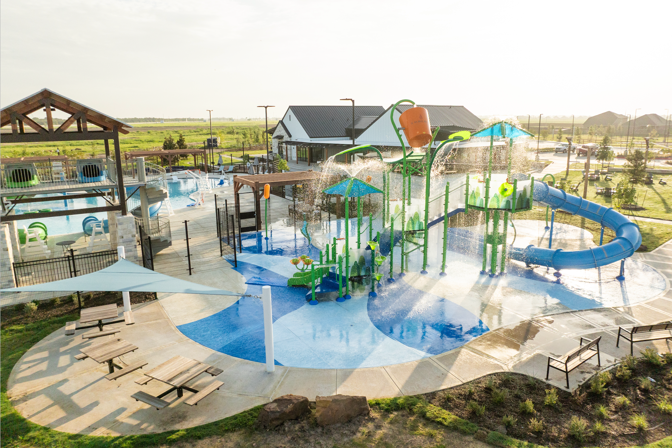 Vibrant splash pad at Emberly in Beasley Texas with green water towers blue slides spraying fountains and lounge seating