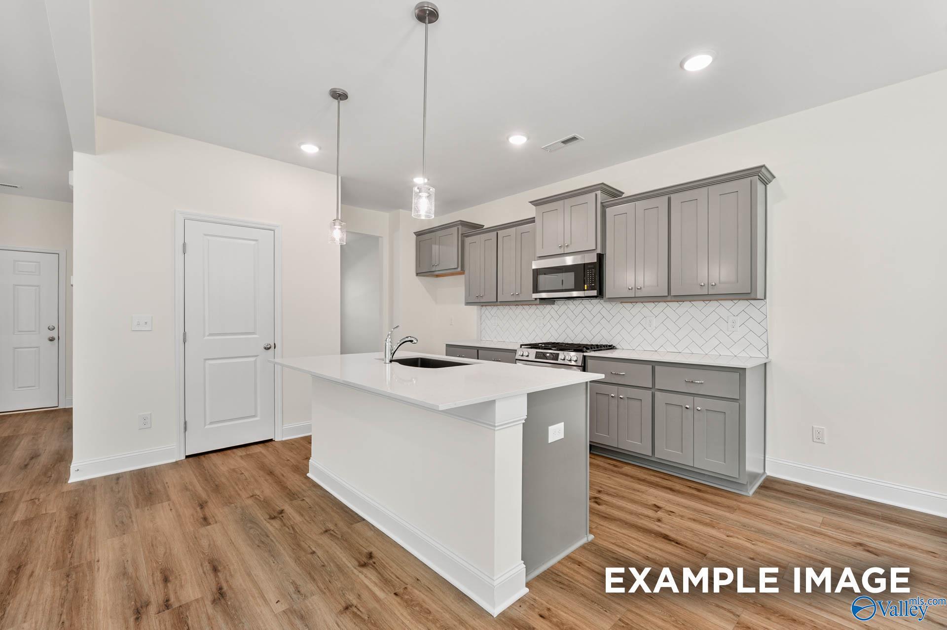 Modern kitchen with gray cabinets, quartz island, and herringbone backsplash in The Shelby A home, Ricketts Farm, Athens.