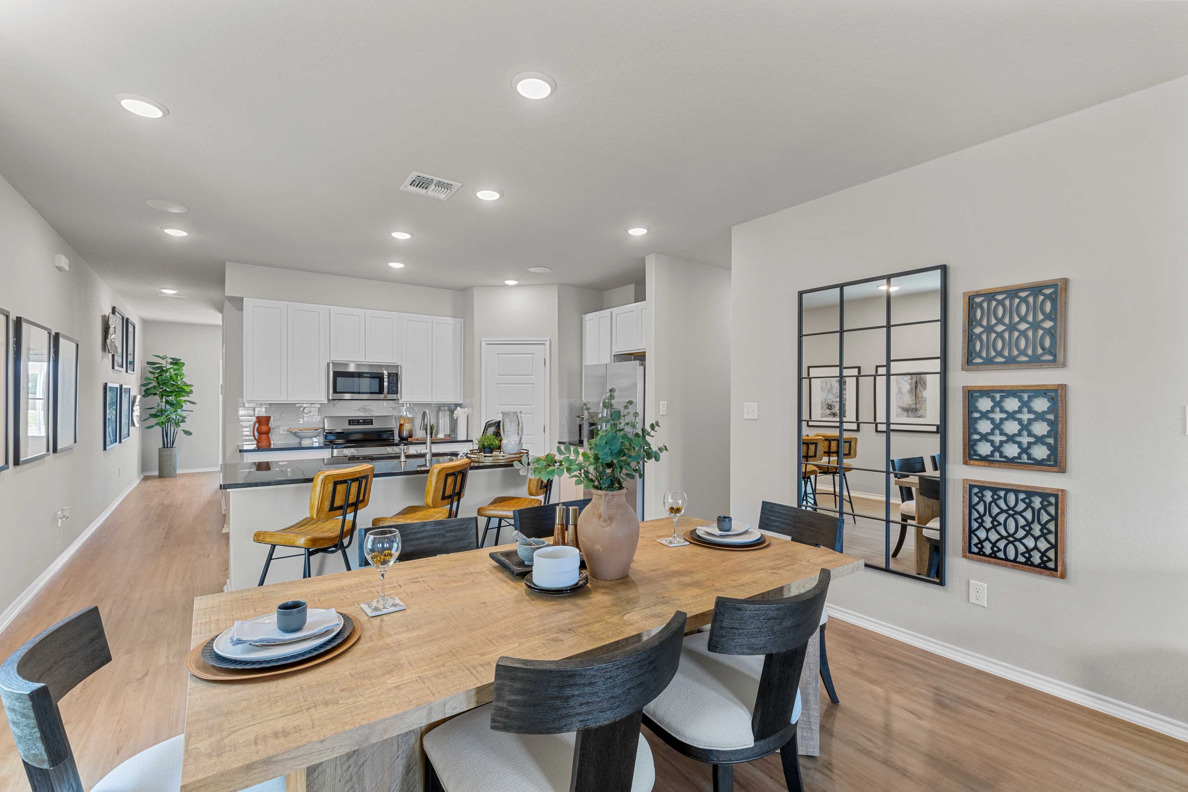 Spacious dining area in The Sabine C home with wooden table, upholstered chairs, open to white kitchen cabinets and plants