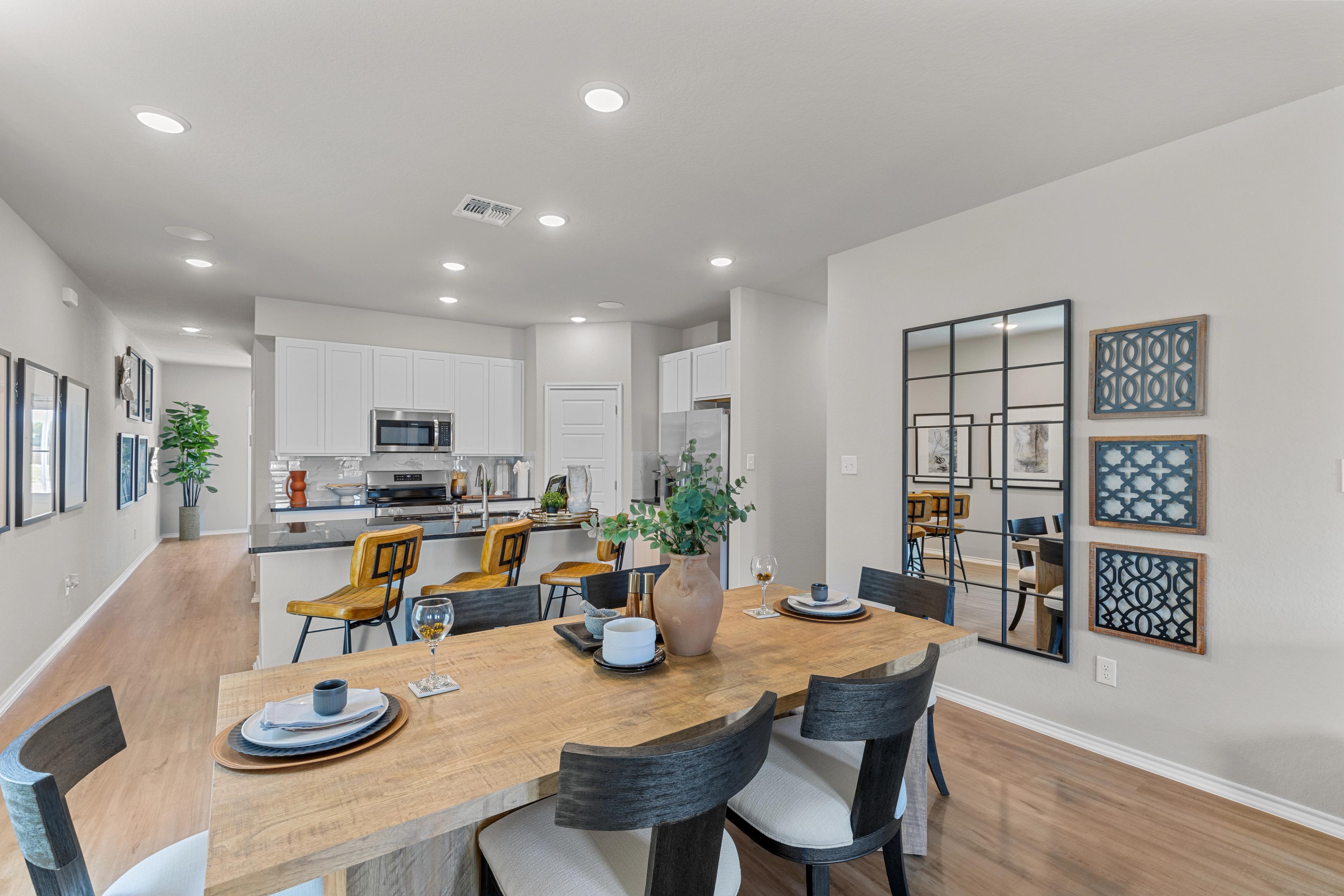 Open-concept kitchen dining area in The Sabine B, white cabinets, stainless appliances, wooden table with chairs, potted plants