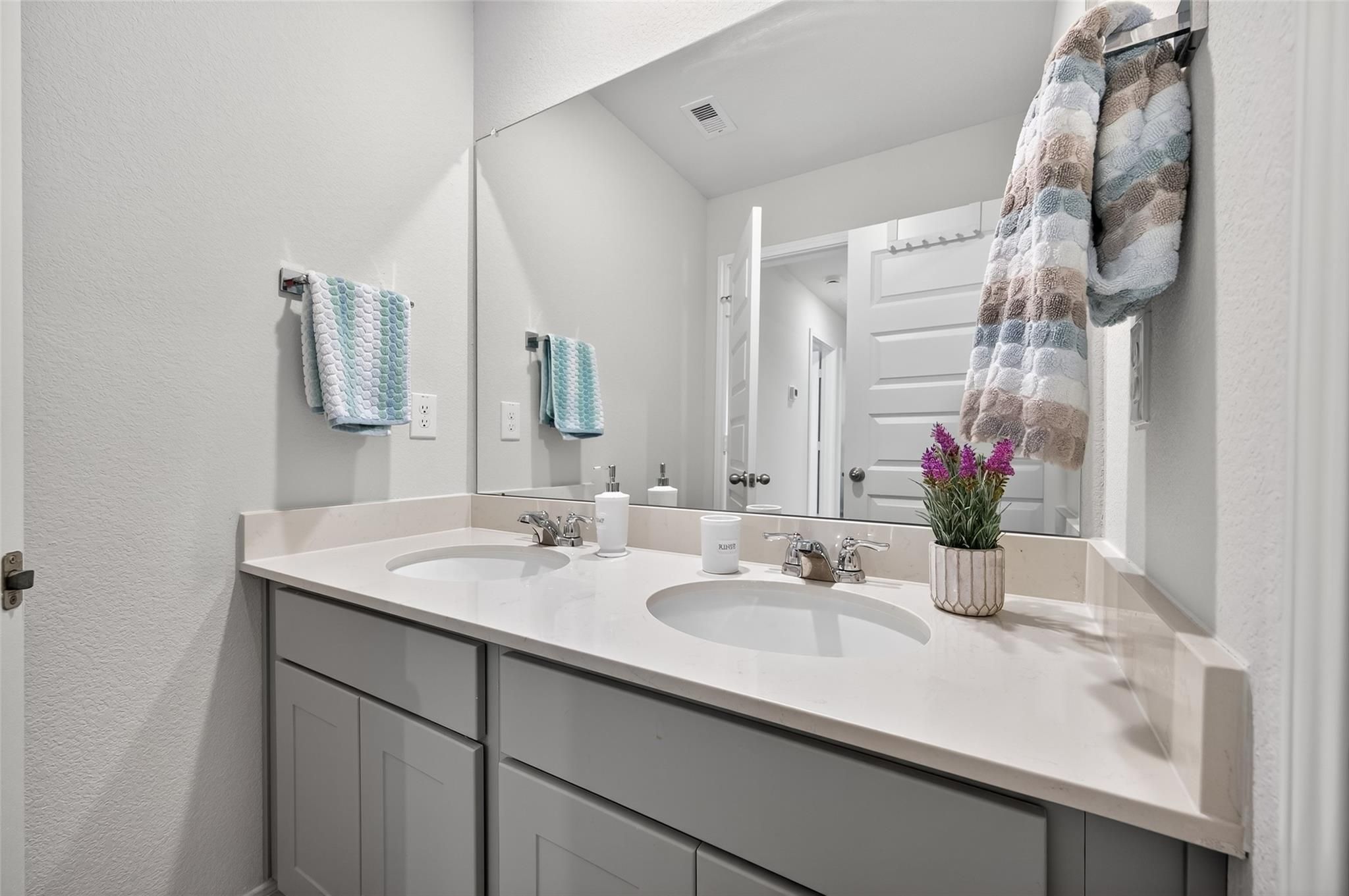 Modern double vanity bathroom with dual sinks, gray cabinets, mirrors, and potted plant in Davidson Homes The Brazos E, Magnolia, Texas