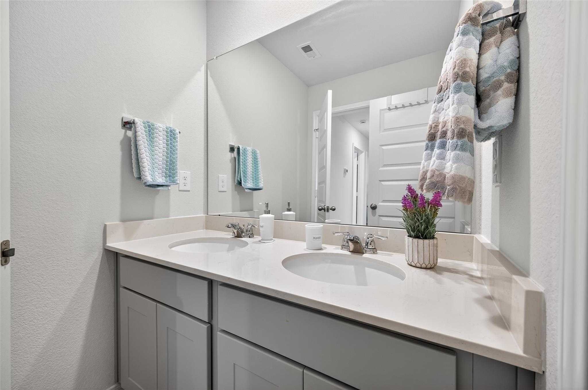 Modern double vanity bathroom with dual sinks, gray cabinets, mirrors, and potted plant in Davidson Homes The Brazos E, Magnolia, Texas