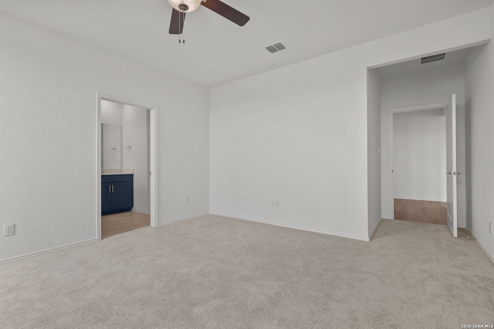 Spacious master bedroom with ceiling fan, beige carpet, and adjacent bath featuring navy vanity in Davidson Homes The Glenwood E, Elmendorf, Texas