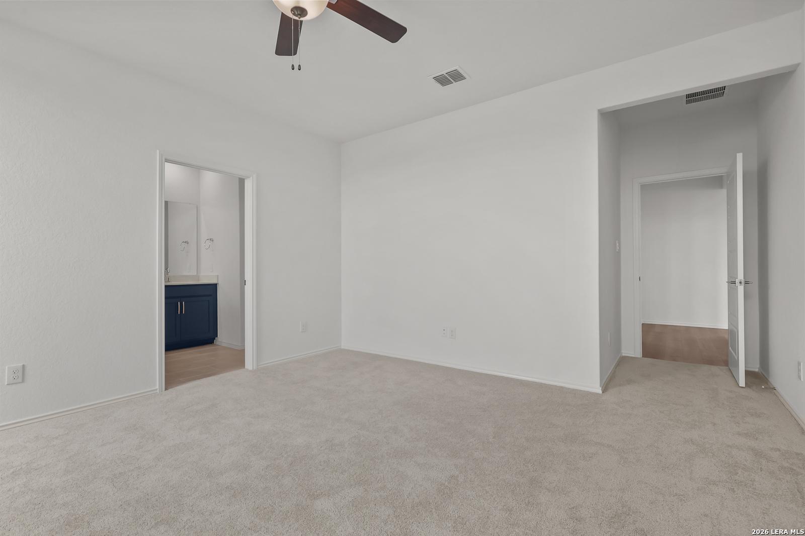 Spacious master bedroom with ceiling fan, beige carpet, and adjacent bath featuring navy vanity in Davidson Homes The Glenwood E, Elmendorf, Texas