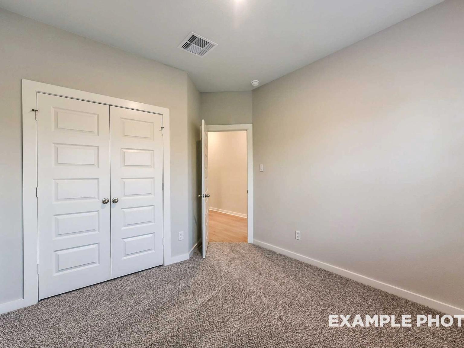 Secondary bedroom with neutral carpet and closet in The Brookside F floor plan at Enclave at Newport, Crosby, Texas.