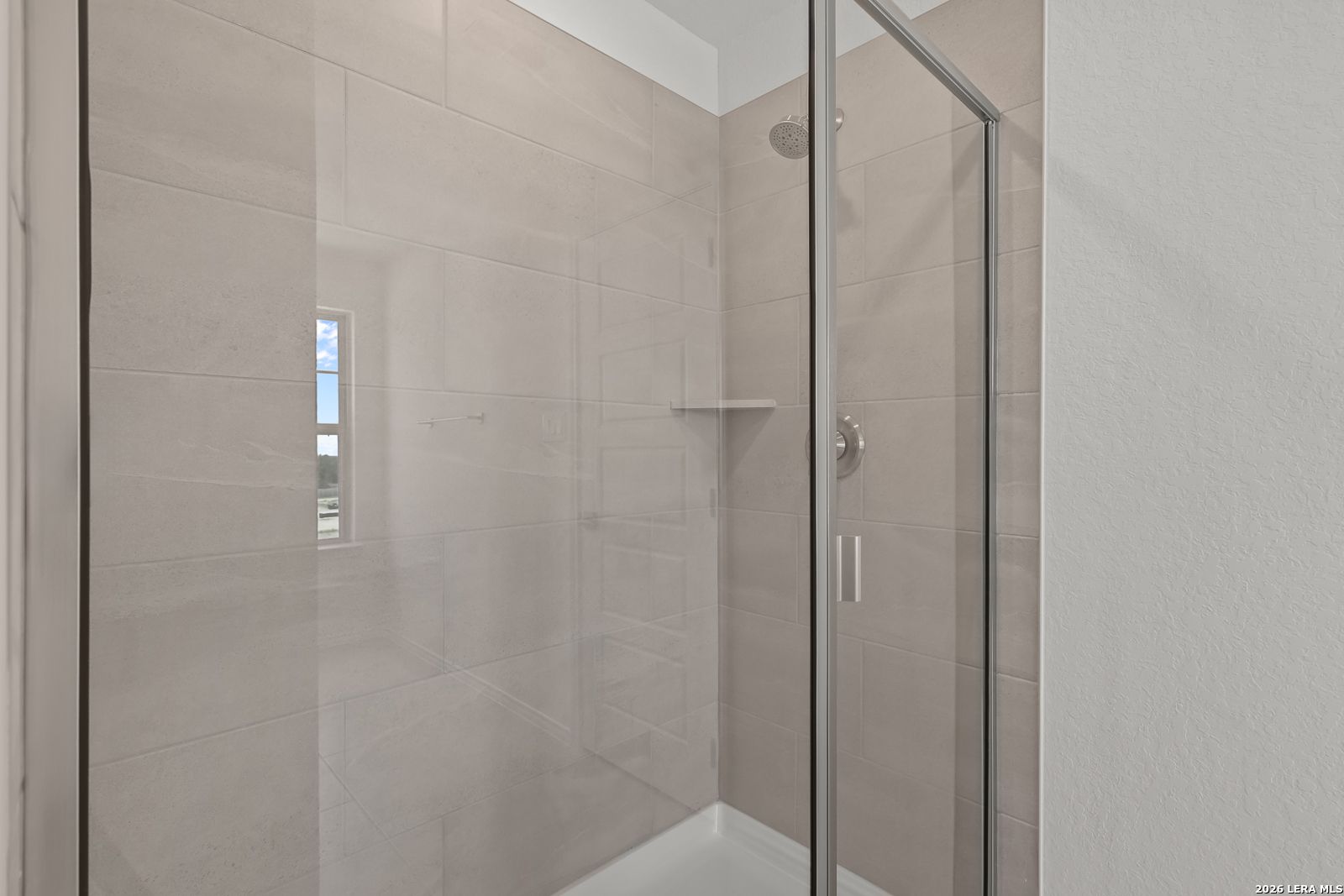 Modern walk-in shower with neutral tile and glass door in The Gillian C floor plan at Meadows at Oak Creek, San Antonio.