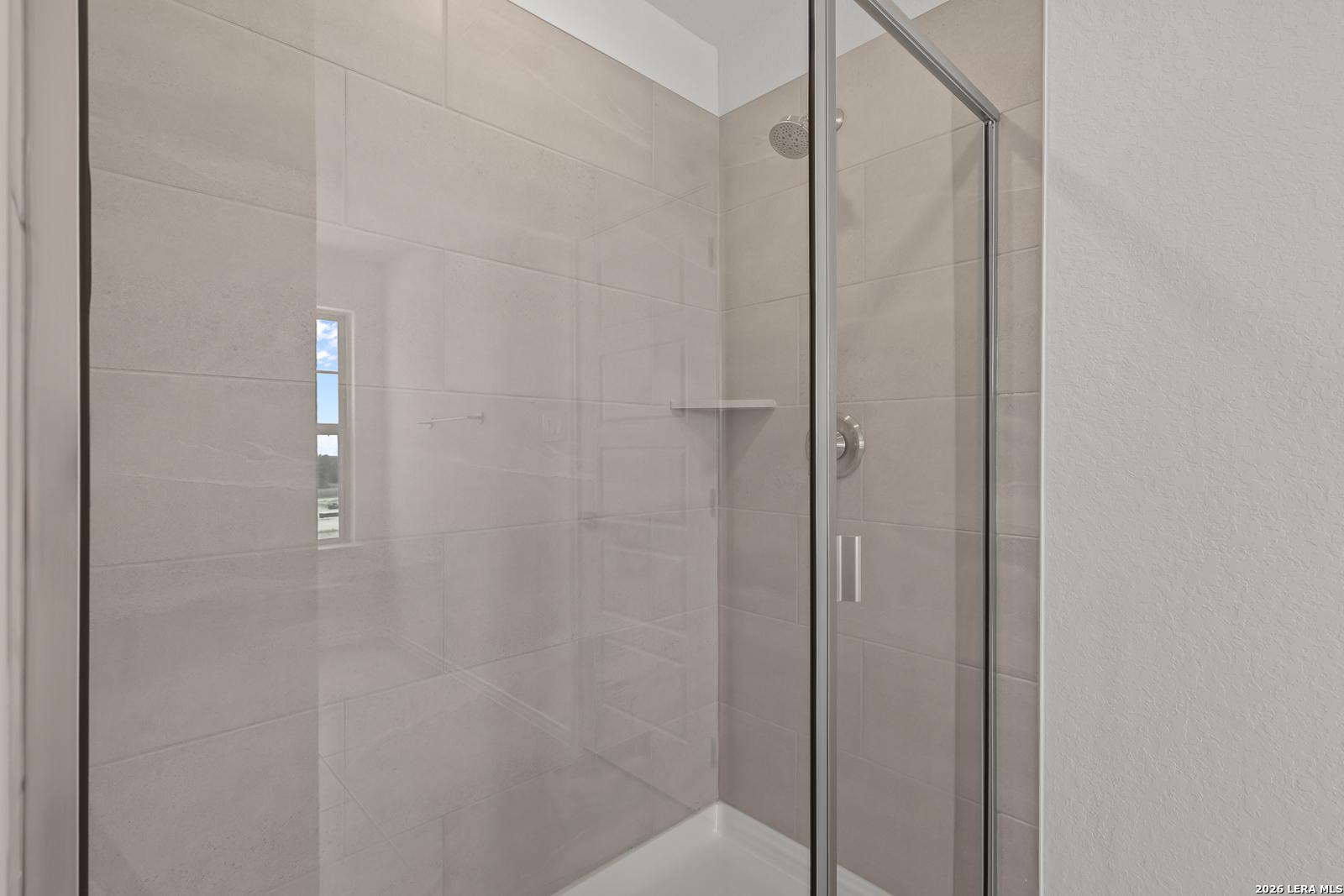 Modern walk-in shower with neutral tile and glass door in The Gillian C floor plan at Meadows at Oak Creek, San Antonio.