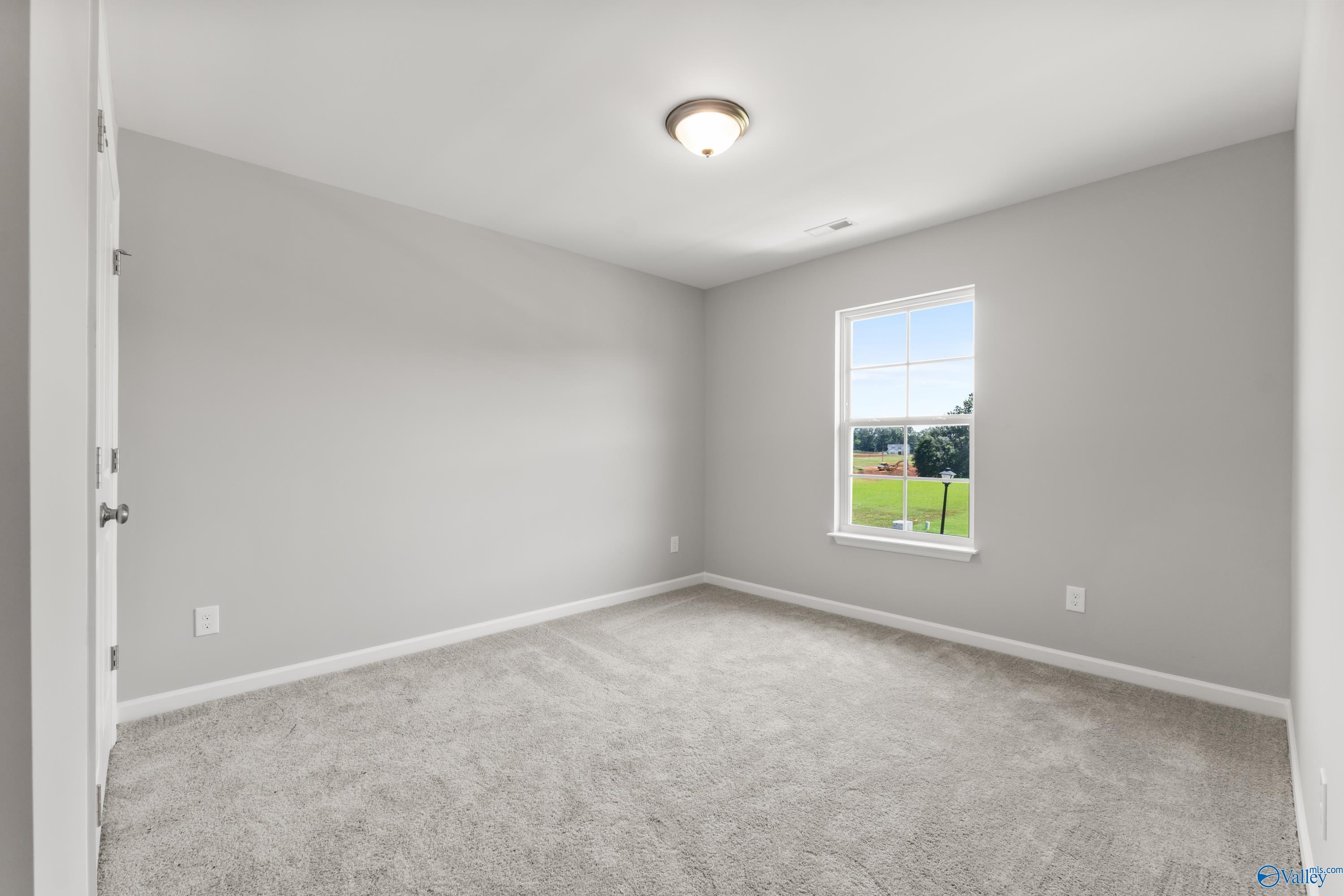 Cozy bedroom with light gray walls, plush carpet, and window overlooking green field in Davidson Homes The Charm, Huntsville AL