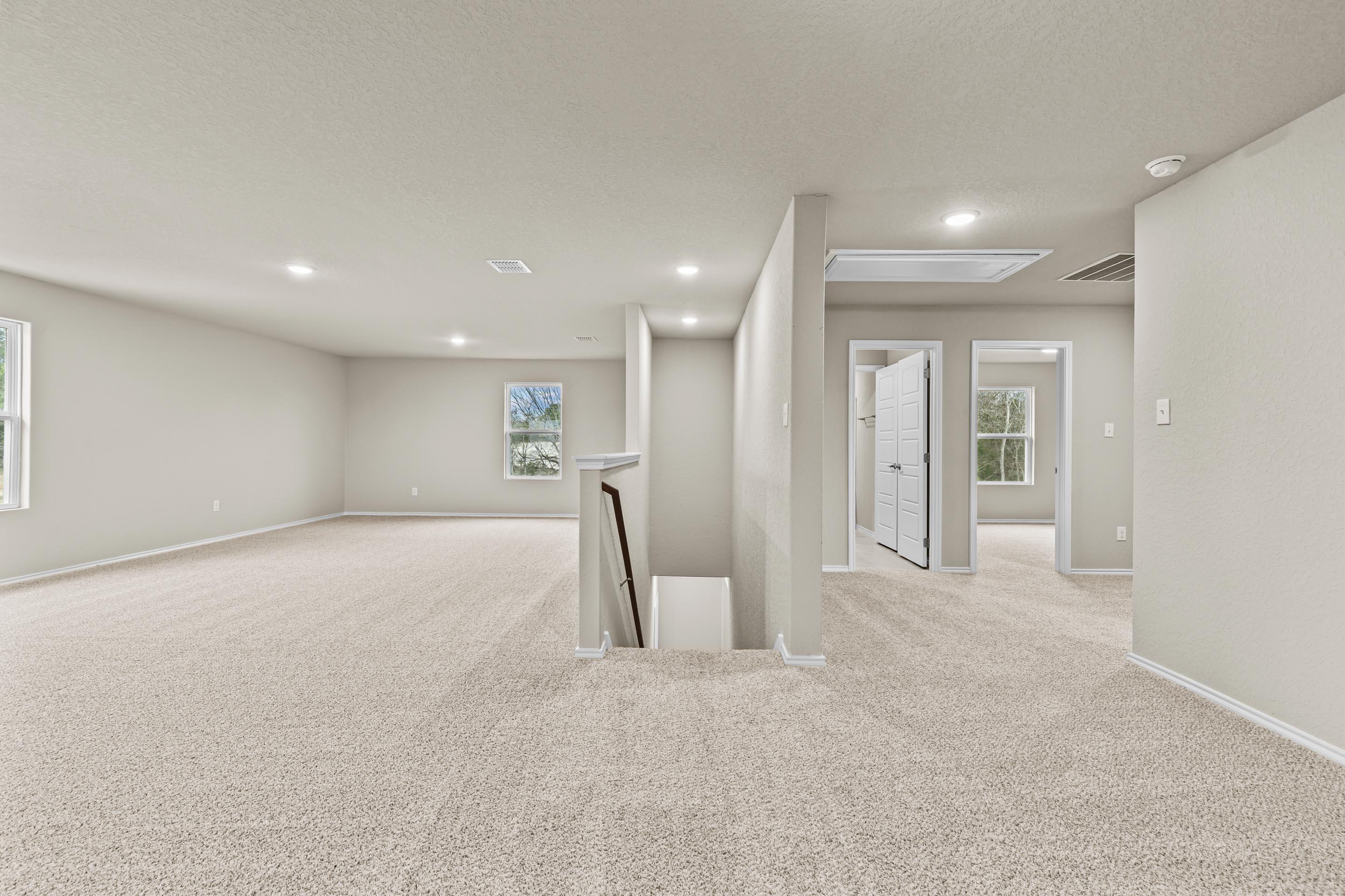 Spacious upstairs loft with beige walls, carpeted flooring, bedroom doors, and staircase in Davidson Homes The Douglas F, San Antonio