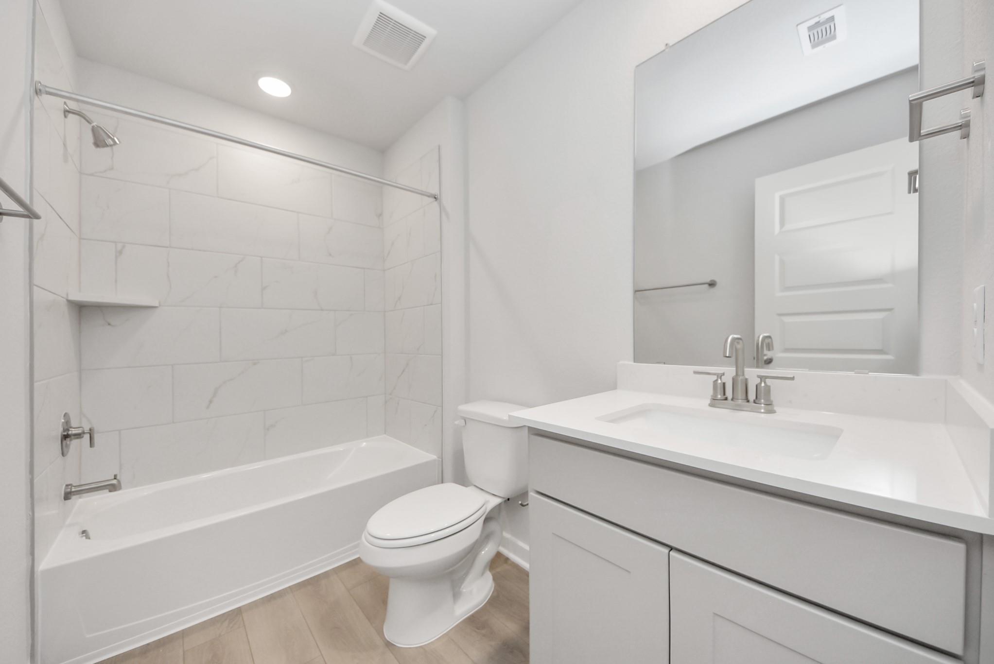 Modern bathroom with white vanity, quartz countertop, and marble-look tiled tub surround in The Verano B, Sunterra, Katy.