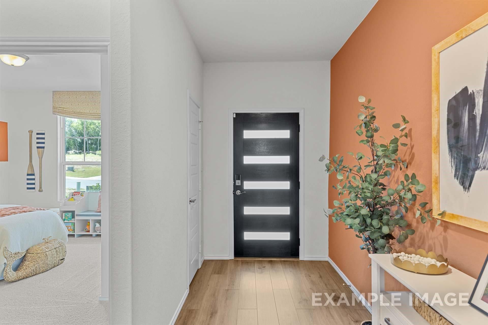 Modern entryway with black front door, accent wall, and wood flooring in The Daphne F home at Sundance Cove in Crosby, TX.