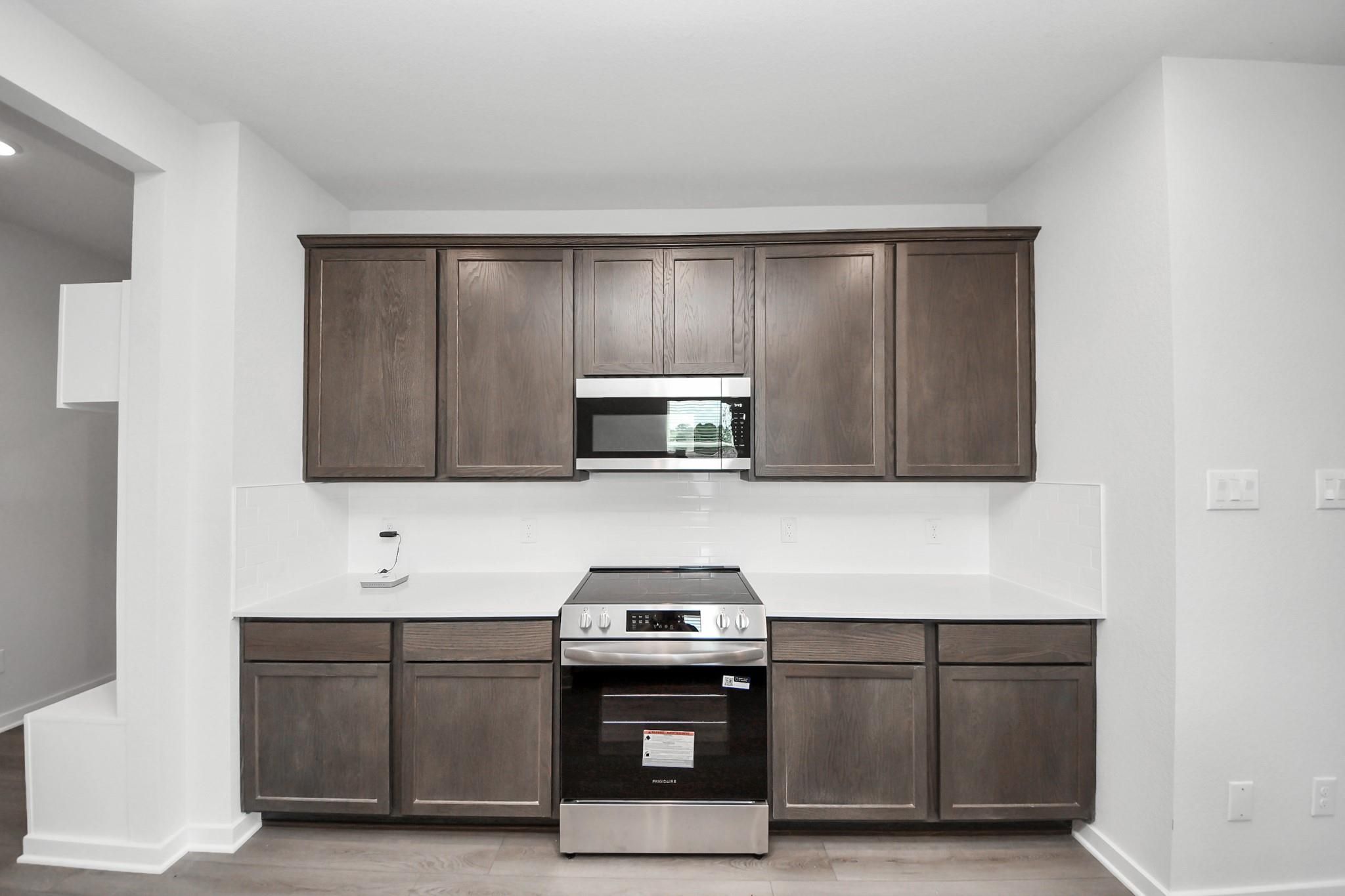 Modern kitchen with dark wood cabinets, white countertops, and stainless appliances in The Brazos F, Cleveland, Texas.