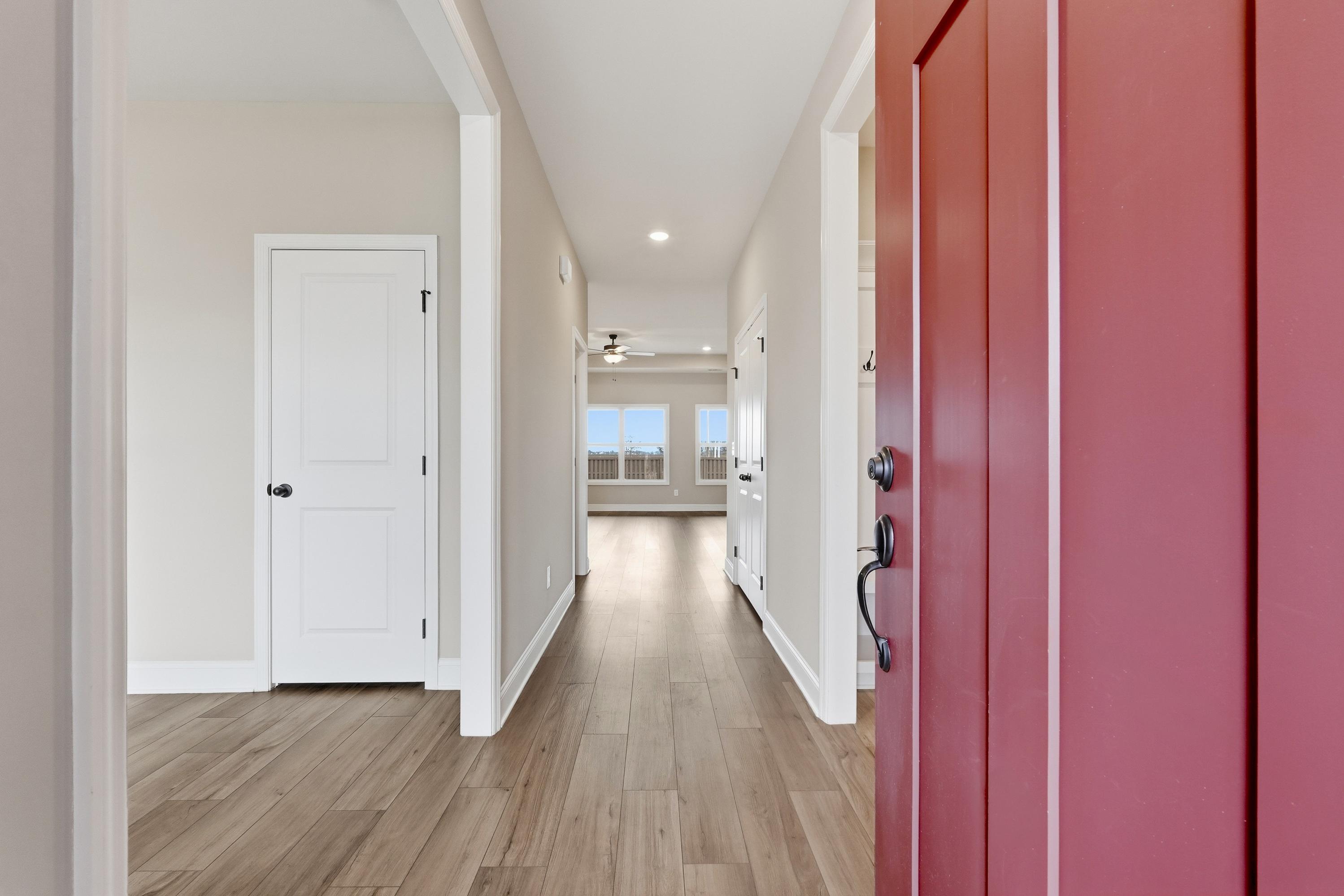 Bright hallway in The Rockford home with hardwood floors, arched doorways, white interior doors, and red entry door