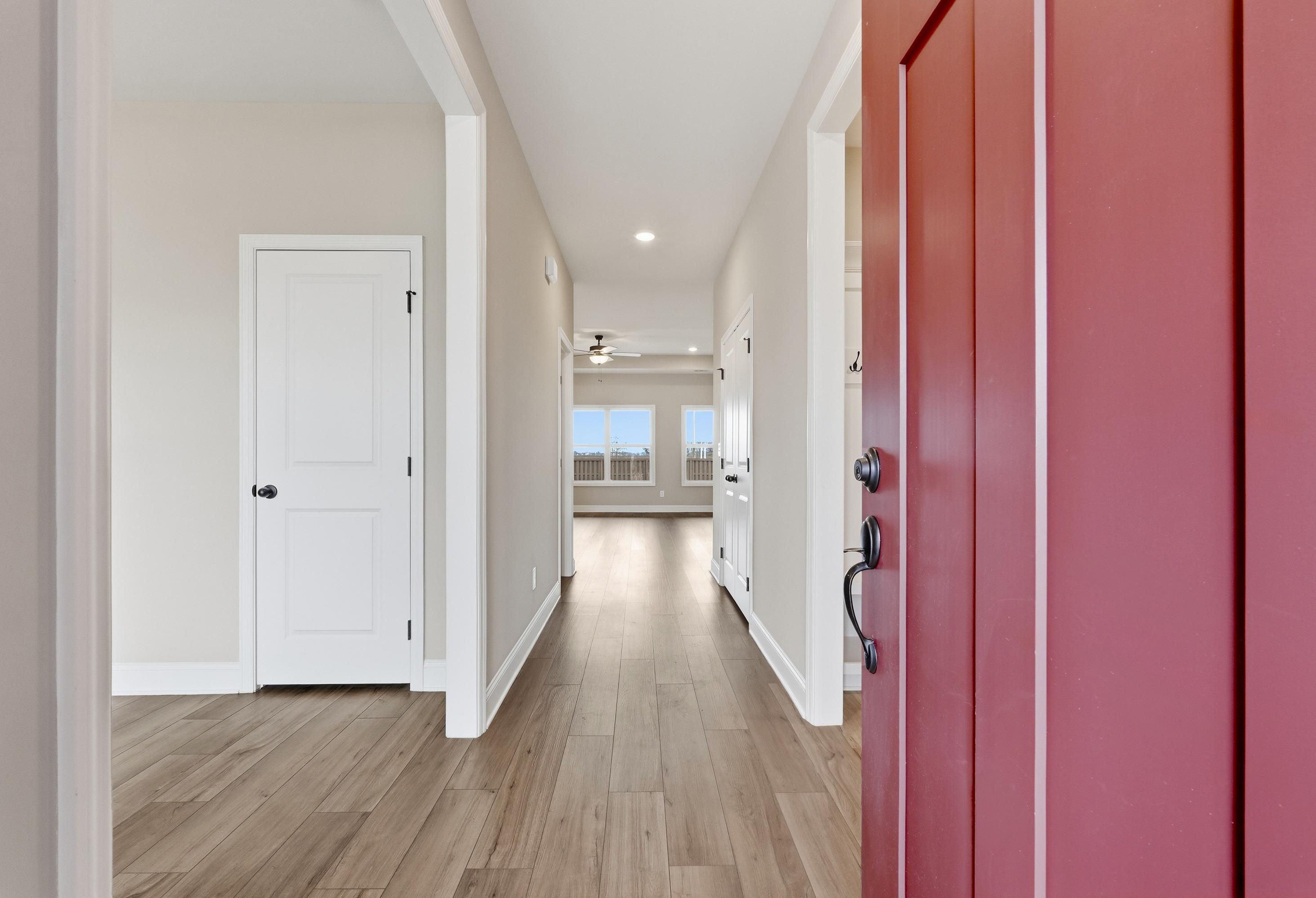Bright hallway in The Rockford home with hardwood floors, arched doorways, white interior doors, and red entry door