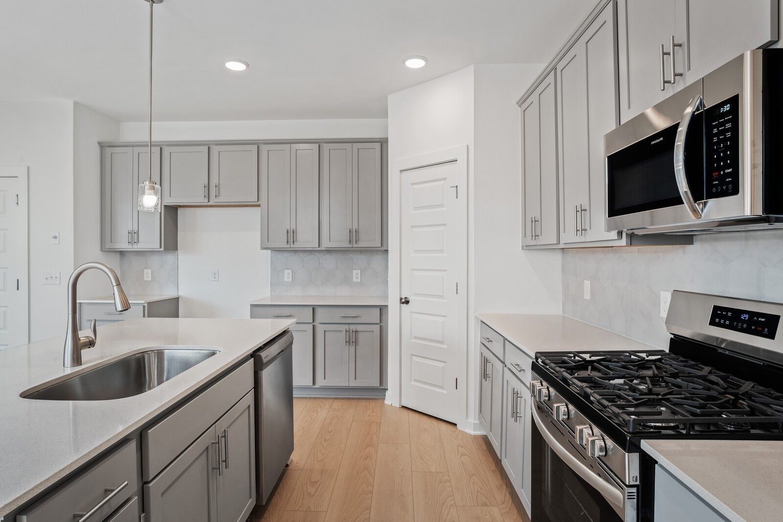Modern kitchen with gray cabinets, quartz countertops, and stainless appliances in The Logan C home at Calista Farms.