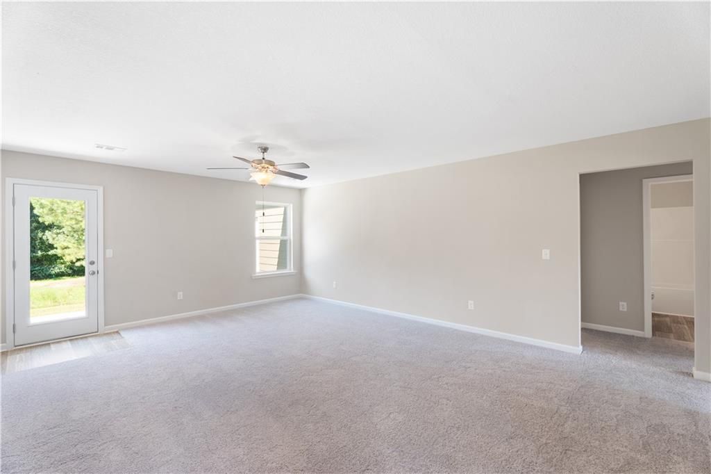 Spacious empty living room with beige walls, carpet flooring, ceiling fan, and glass door to green backyard in Davidson Homes The Washington, Phenix City