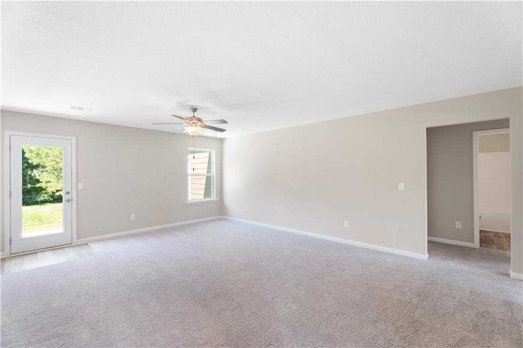 Spacious empty living room with beige walls, carpet flooring, ceiling fan, and glass door to green backyard in Davidson Homes The Washington, Phenix City