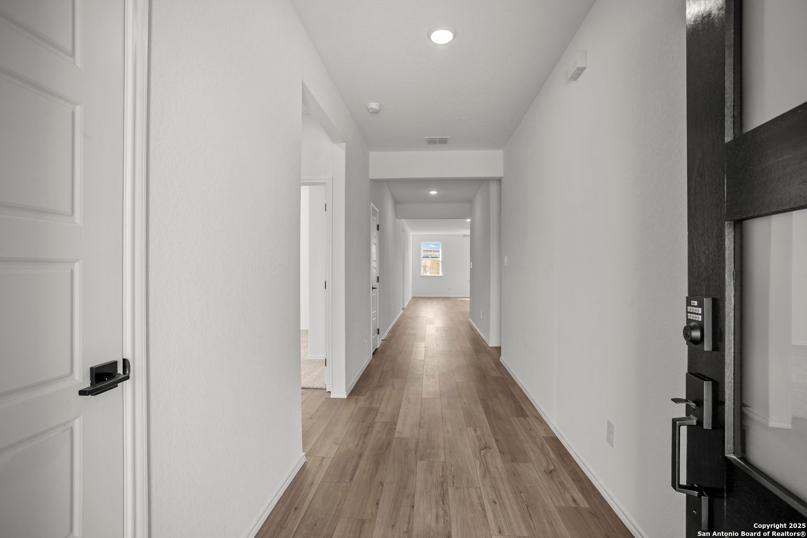 Bright hallway with light hardwood floors and white walls in The Daphne K 4-bedroom home by Davidson Homes, San Antonio