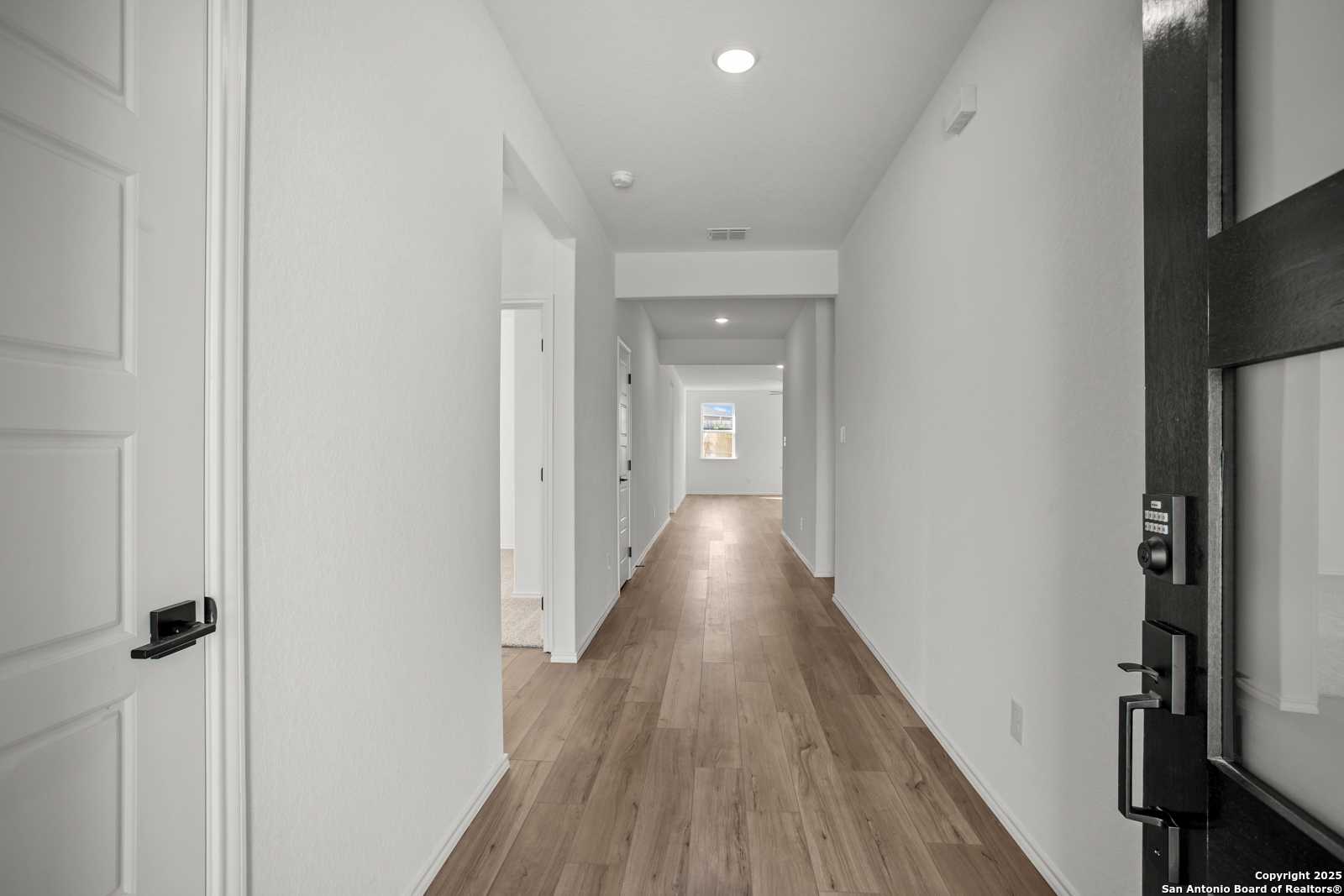 Bright hallway with light hardwood floors and white walls in The Daphne K 4-bedroom home by Davidson Homes, San Antonio