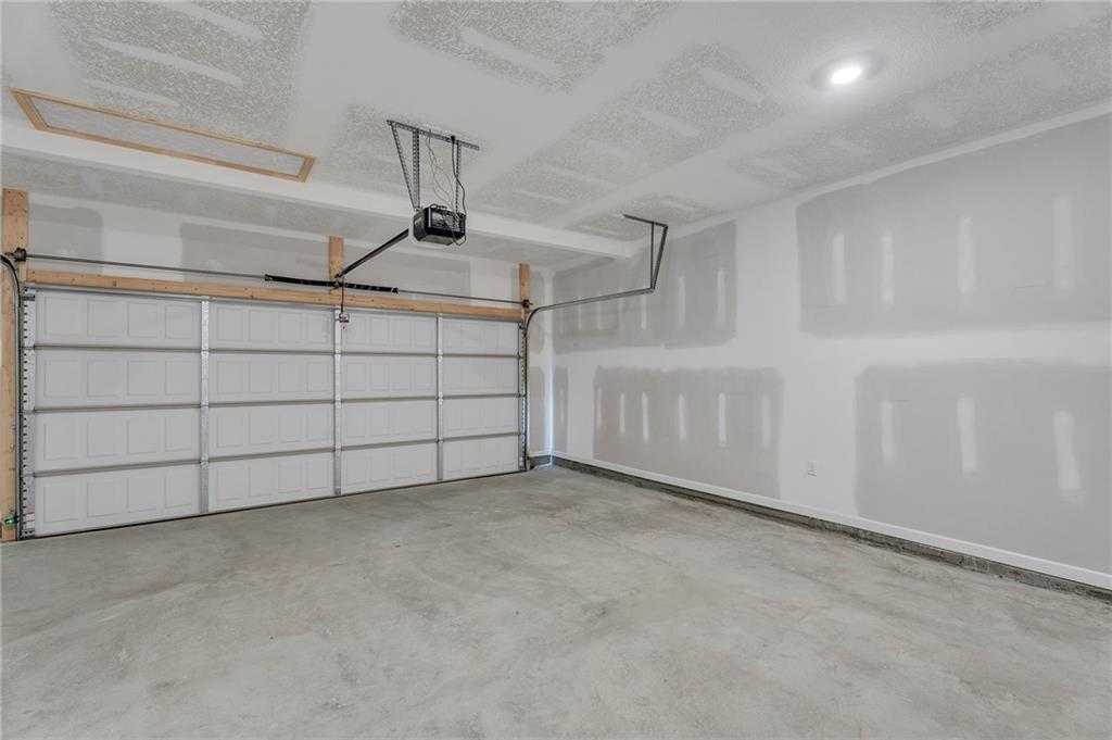 Spacious 2-car garage with open doors, unfinished drywall walls, and exposed ceiling in Davidson Homes The Bartlett, Phenix City, AL