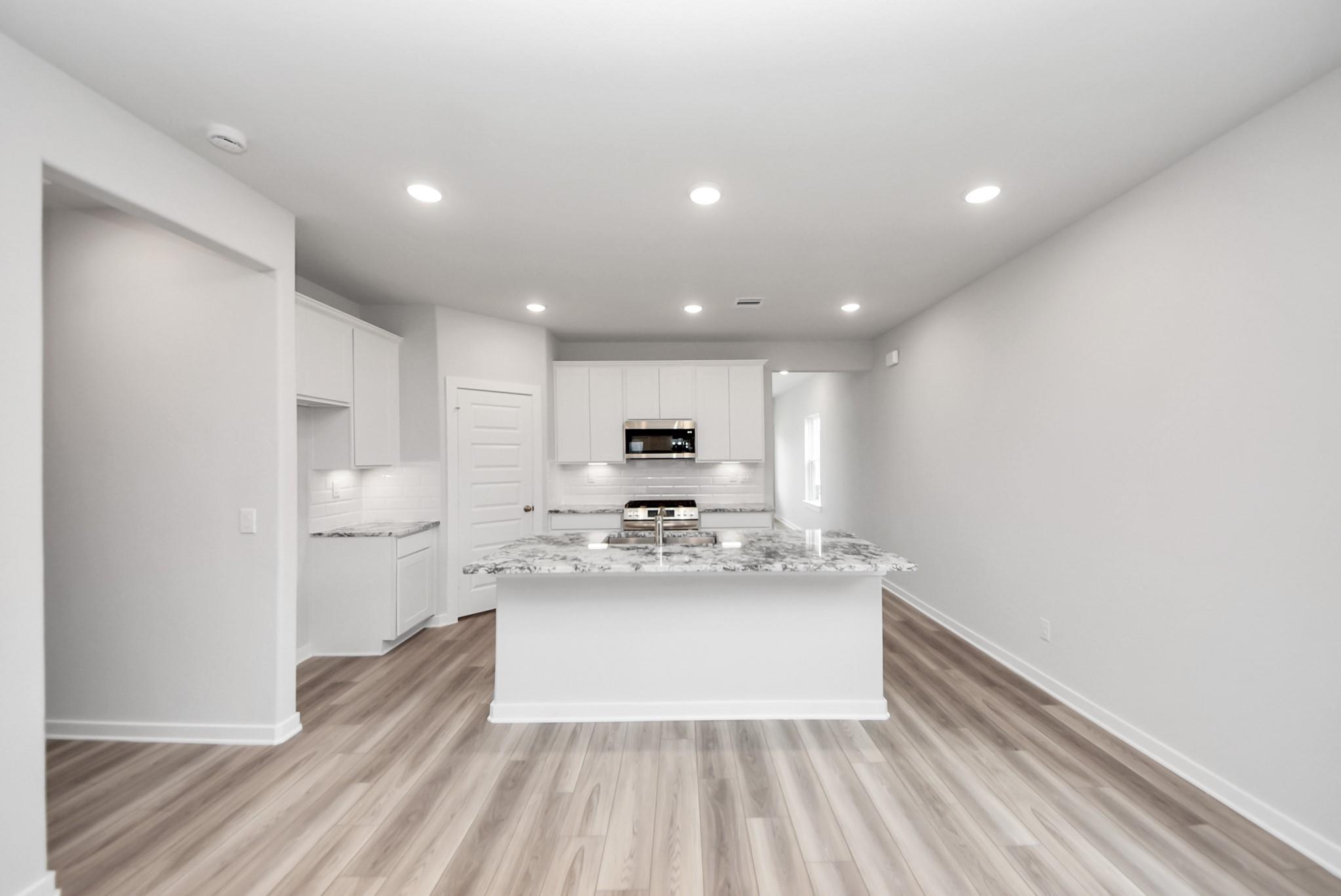 Modern kitchen with white cabinets, granite island, and wood-look floors in The Sabine E floor plan, Magnolia, Texas.