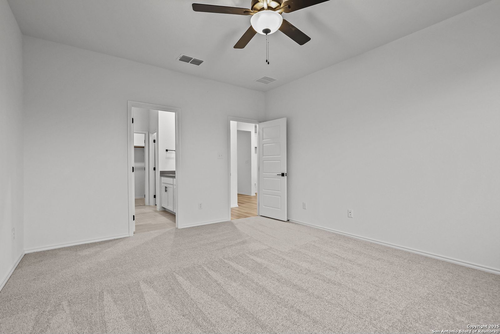 Spacious bedroom with ceiling fan, en-suite bath vanity, and beige carpet in Davidson Homes The Daphne J, Converse, Texas