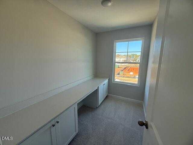 Bright home office with built-in white desk, cabinets, and large window overlooking neighborhood in Davidson Homes The Gavin B, Lillington, NC