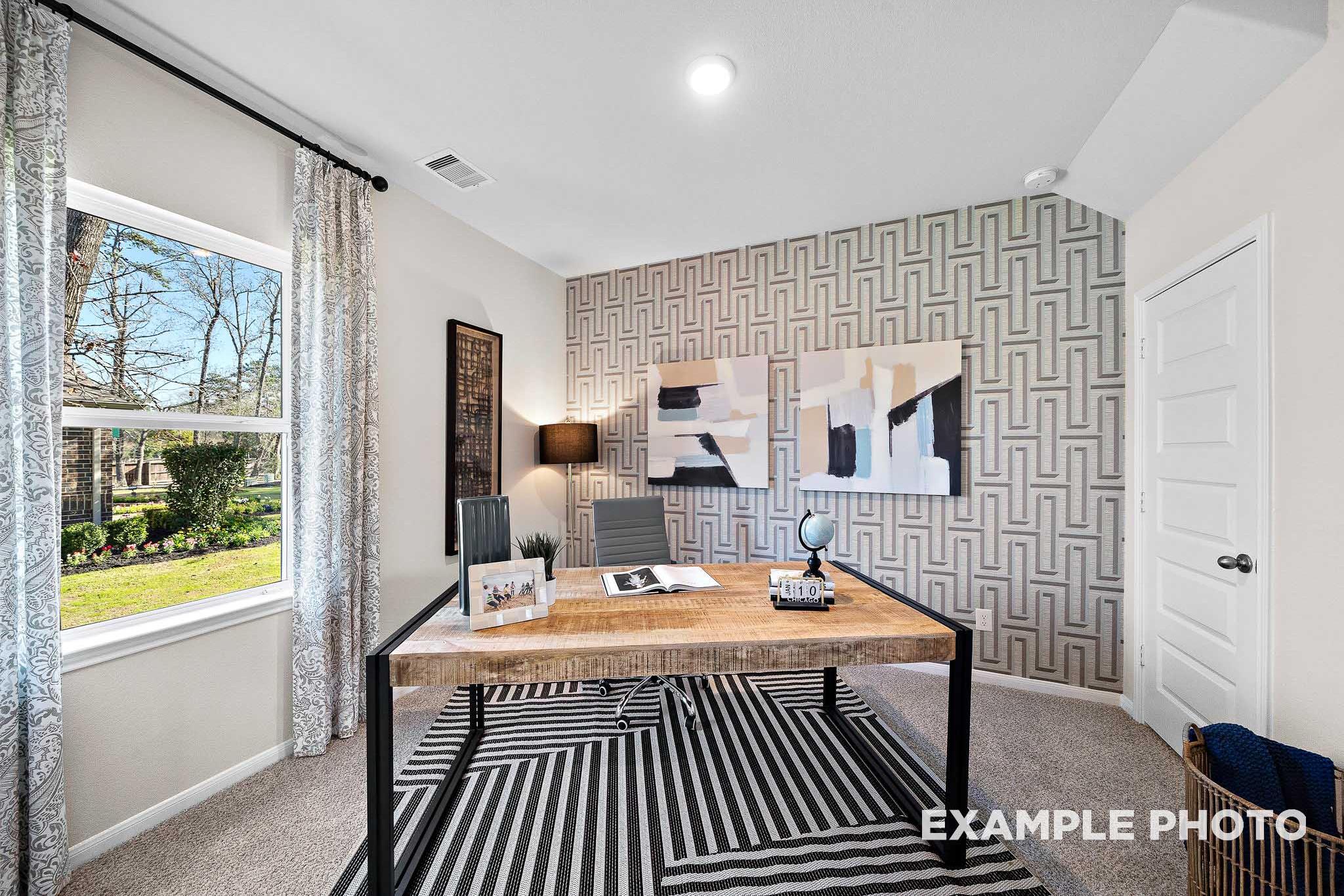 Stylish home office in The San Marcos plan with wooden desk, geometric wallpaper, abstract art, and window views