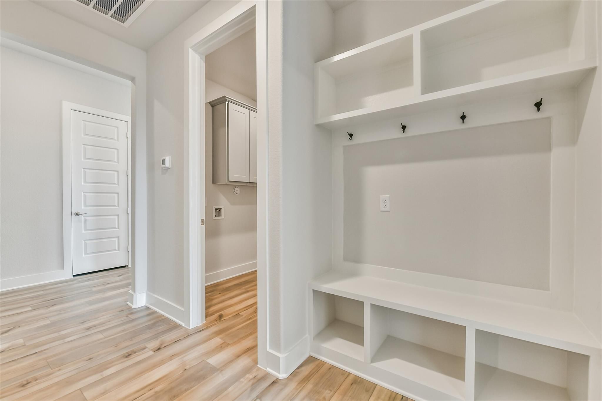 Spacious mudroom with white built-in shelves, bench, coat hooks, and laundry room access in Davidson Homes The George A, Lago Mar, Texas City