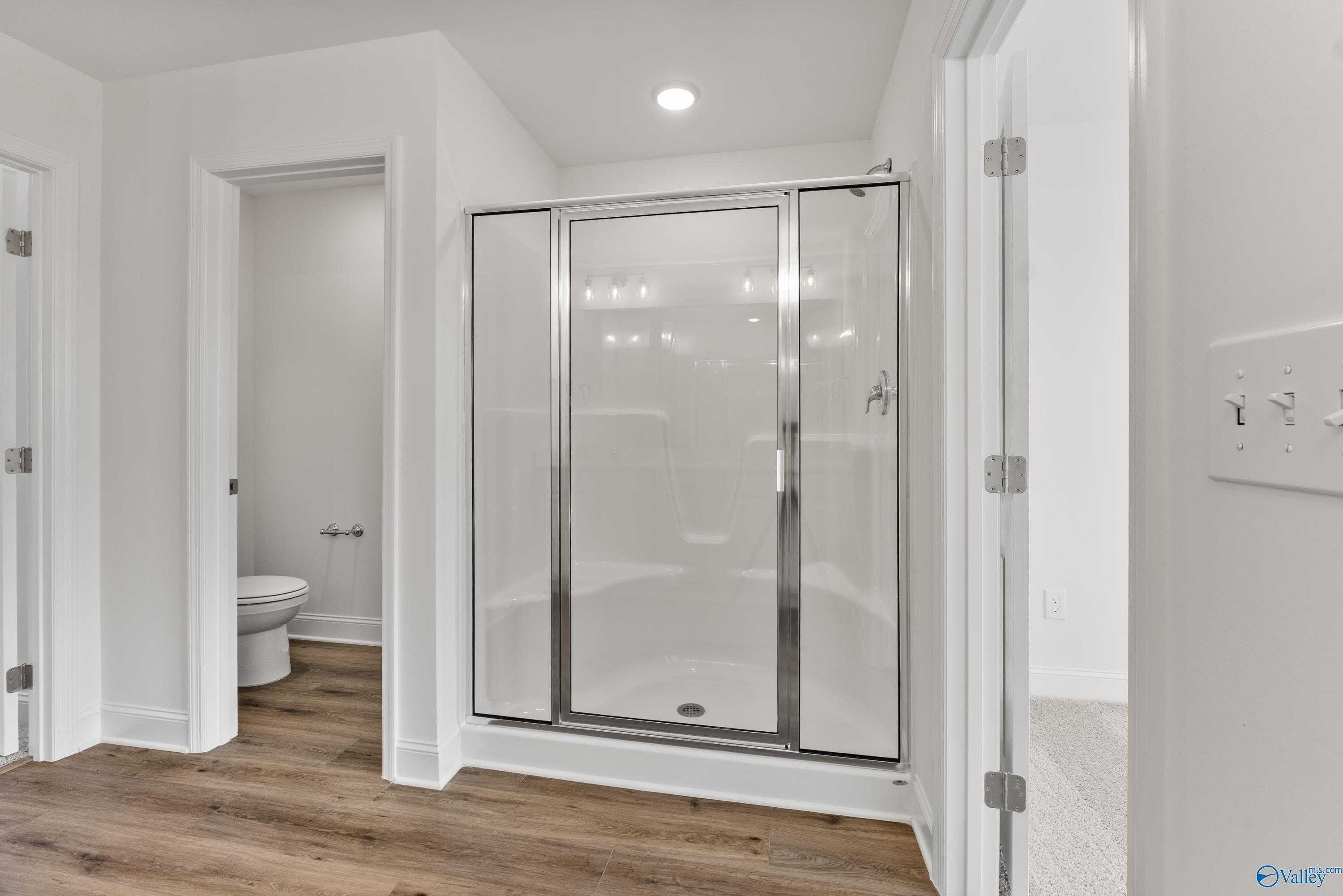 Modern master bathroom featuring frameless glass shower, white tile, and luxury vinyl plank flooring in Davidson Homes The Shelby A, New Market, Alabama