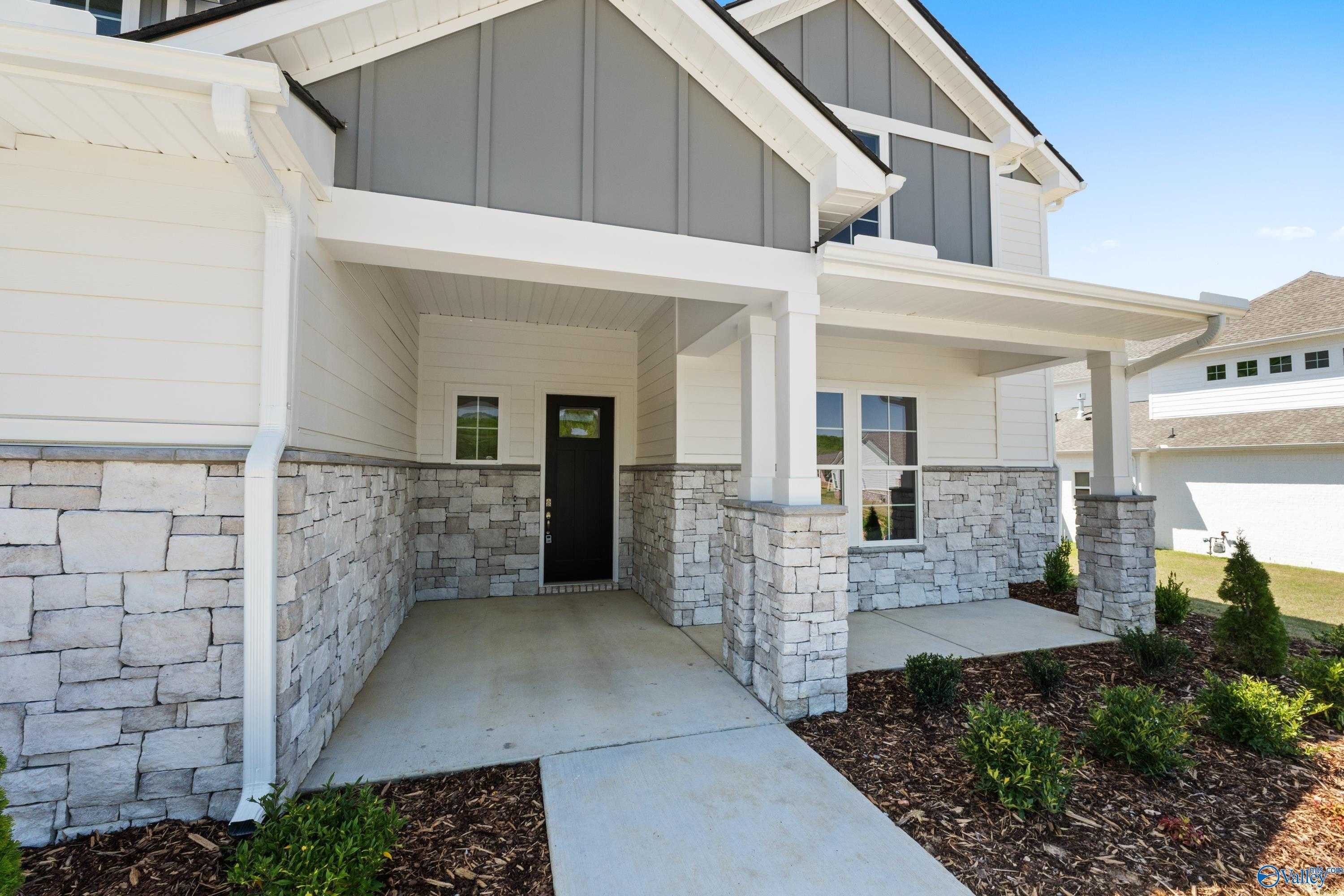 Modern two-story home front with covered porch, stone columns, gray siding, black door in The Meadows at Hampton Cove, Owens Cross Roads, Alabama