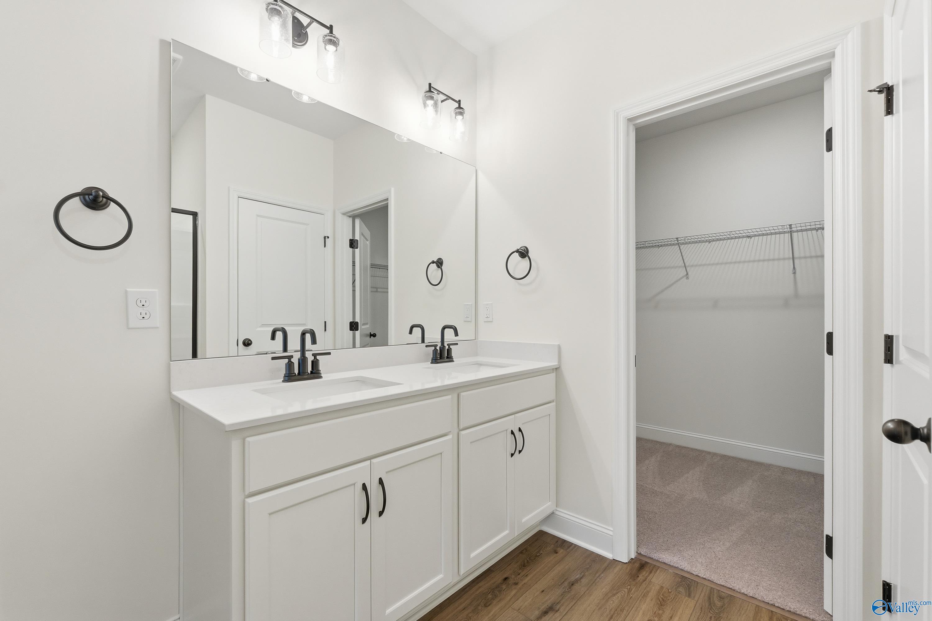 Modern master bathroom featuring double white vanity, large framed mirror, and adjacent walk-in closet in Davidson Homes The Franklin C, New Market, Alabama