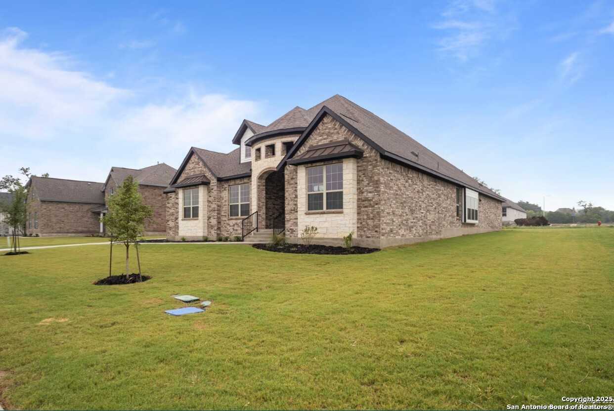 Modern 1-story brick home with stone accents, gabled roof, and landscaped yard in Potranco Oaks, Castroville, Texas