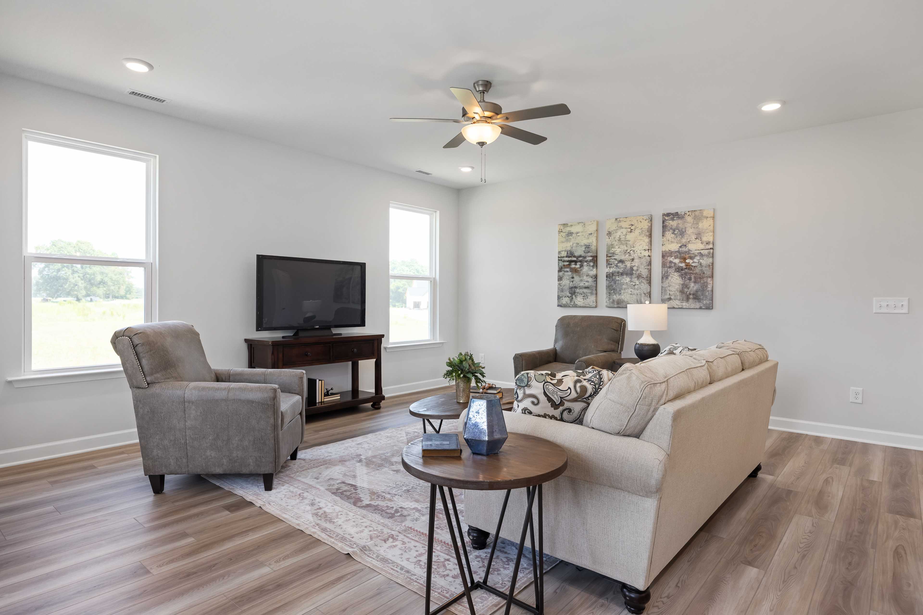 Cozy living room in Woodland Crossing, Zebulon NC with beige sectional sofa, hardwood floors, ceiling fan, and abstract art
