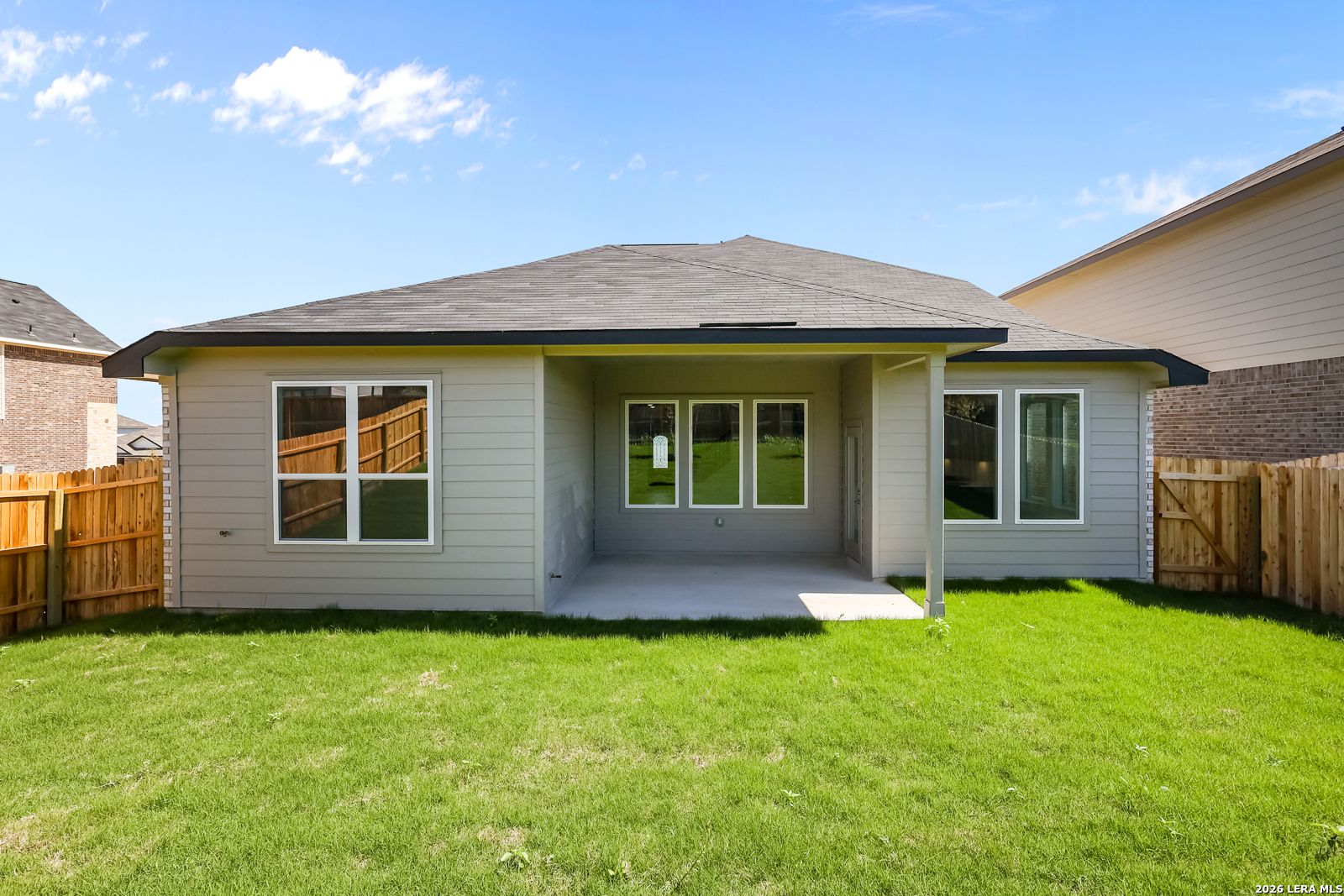 Rear view of two-story Sequoia B home with covered patio, large windows, and fenced green backyard in Comanche Ridge, San Antonio, Texas