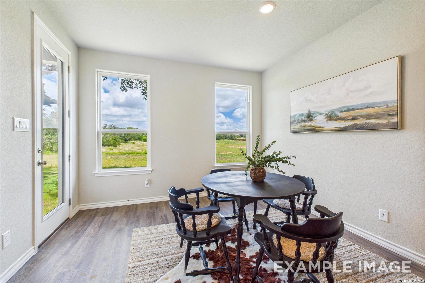 Bright dining nook with round table, wood floors, and scenic backyard views in The Foster F home, Potranco Oaks.