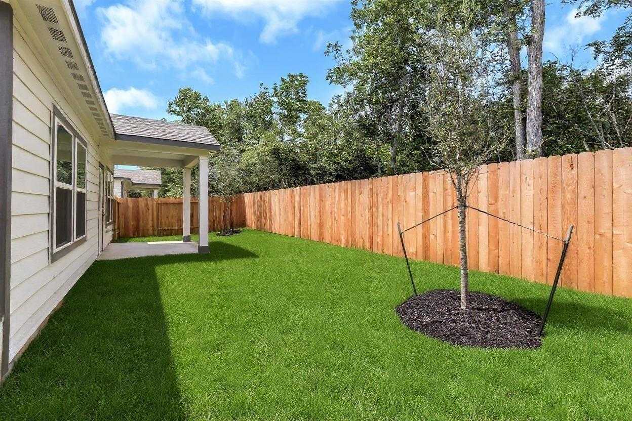 Serene private backyard with lush green lawn, young staked tree, wooden privacy fence, and covered patio in Davidson Homes The Sabine E, Conroe, Texas