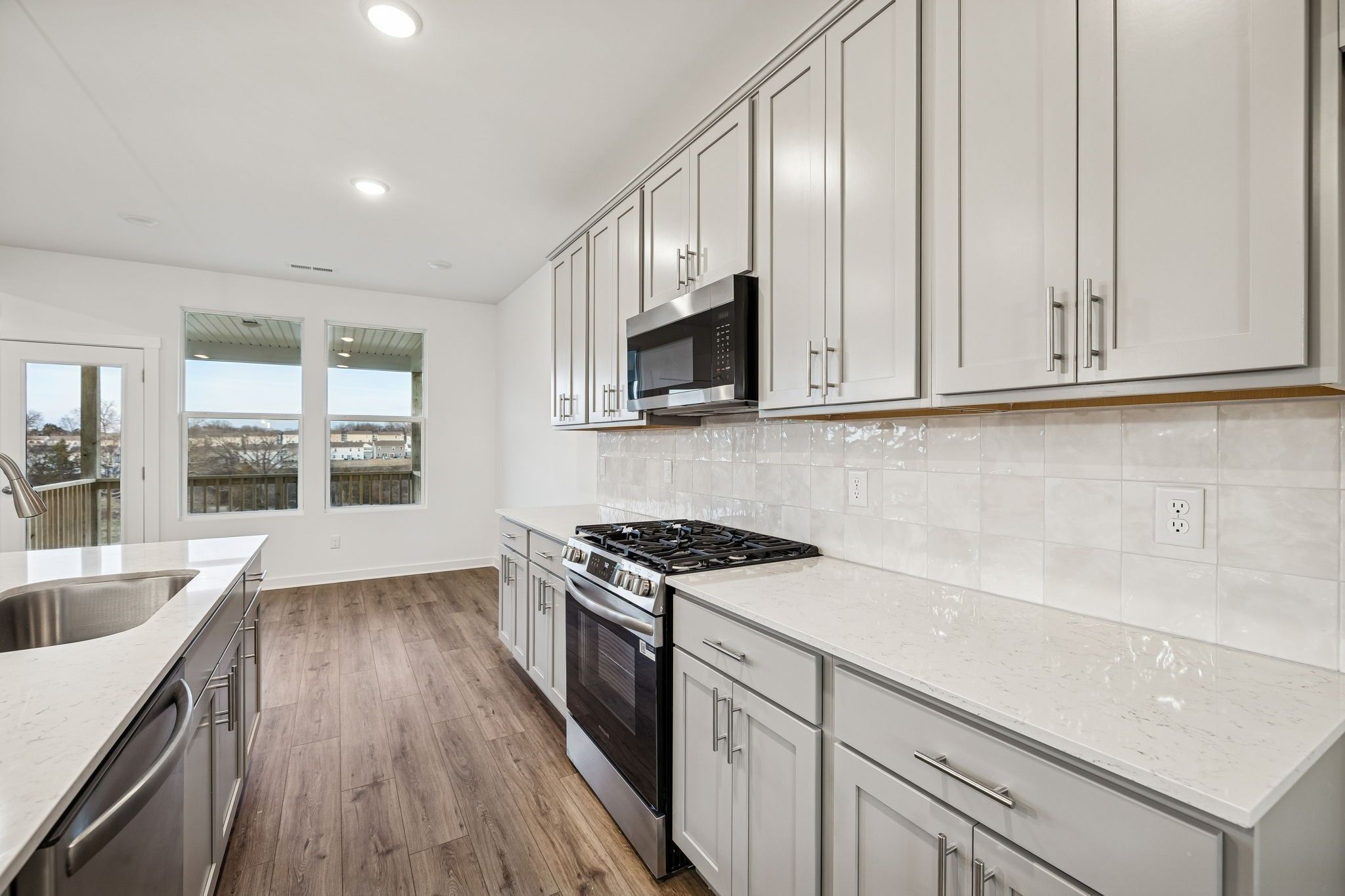 Modern kitchen with white cabinets, gas range, microwave, quartz countertops and hardwood floors in Davidson Homes The Willow B, White House, TN