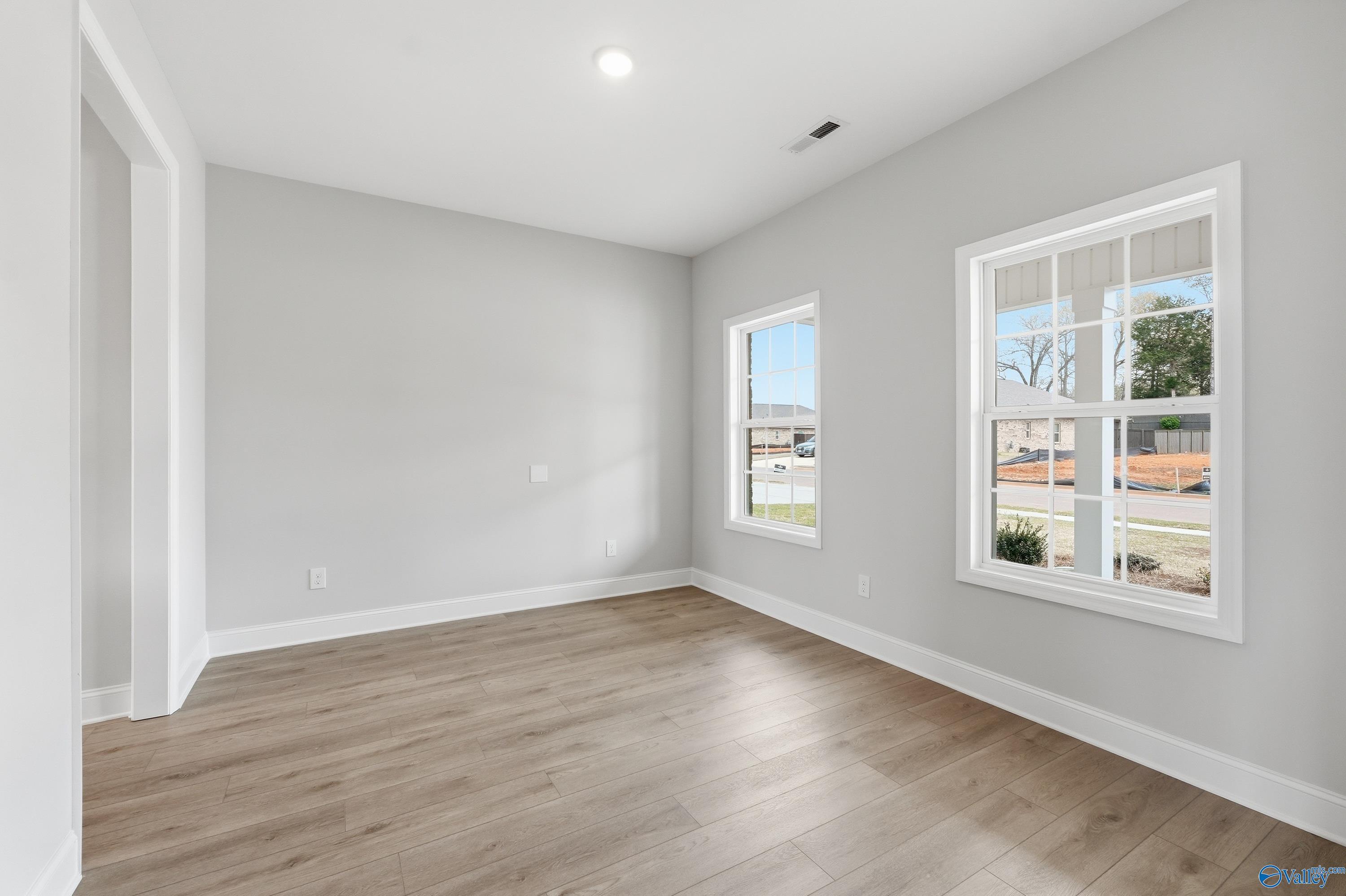 Bright empty bedroom with gray walls, hardwood floors, and large windows overlooking neighborhood in The Shelby B, New Market, AL