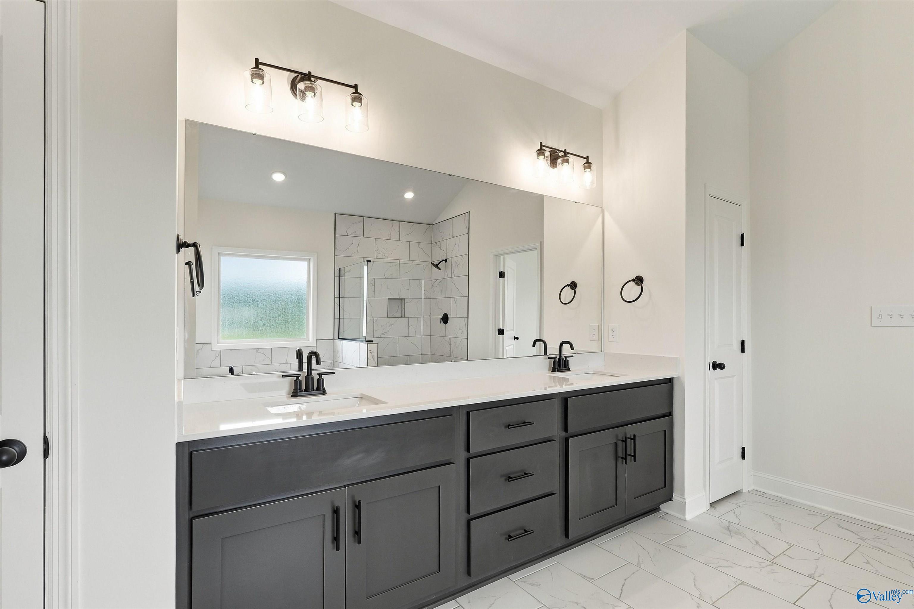 Dual vanity master bath with dark gray cabinets, white quartz counters, matte black fixtures, and tile shower in Davidson Homes' The Valencia, Huntsville