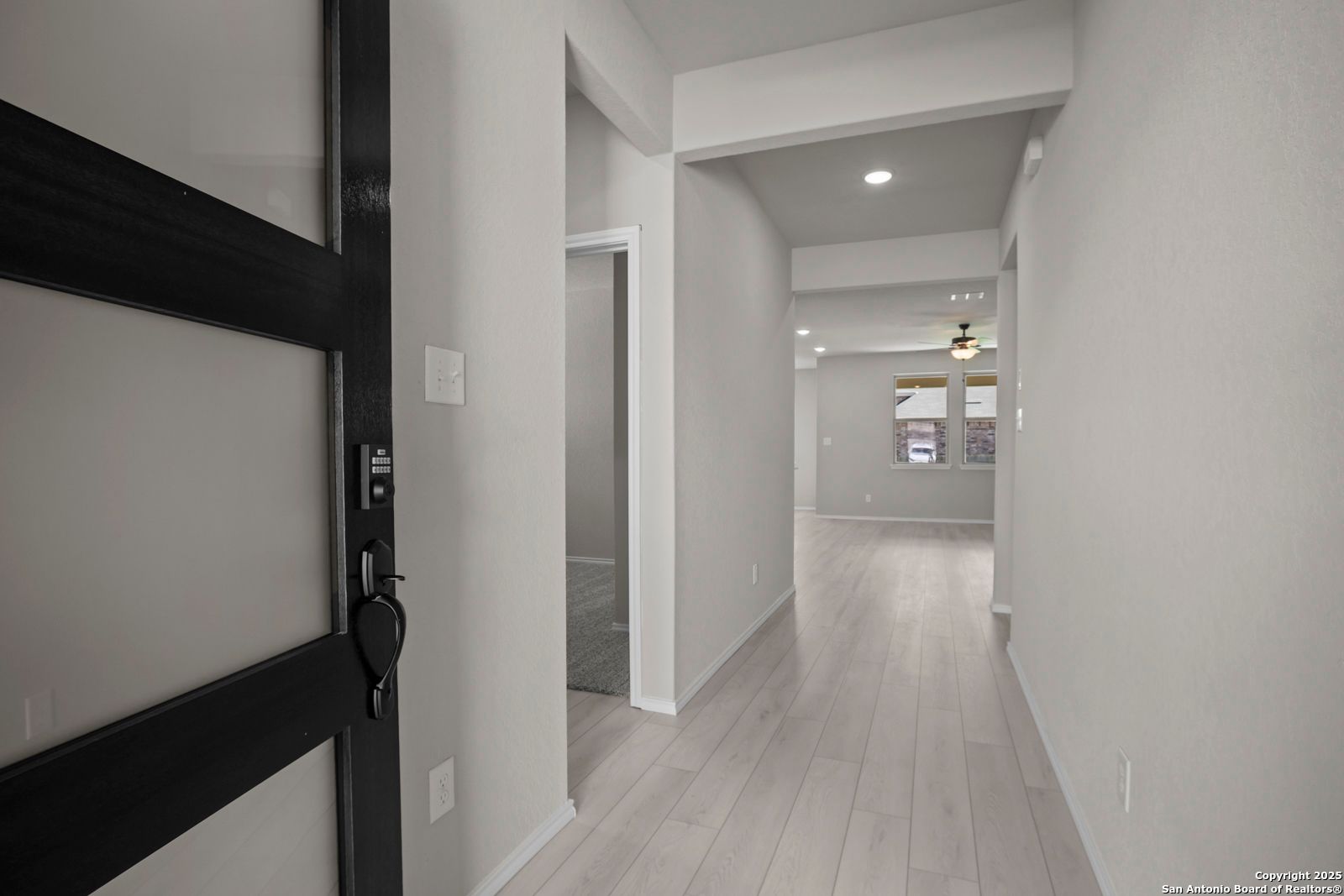 Modern entryway with black front door, light wood floors, and open hallway in The Asheville E 3-bedroom home, Converse, Texas