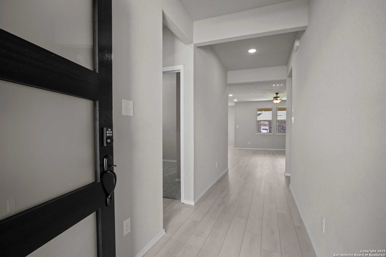Modern entryway with black front door, light wood floors, and open hallway in The Asheville E 3-bedroom home, Converse, Texas