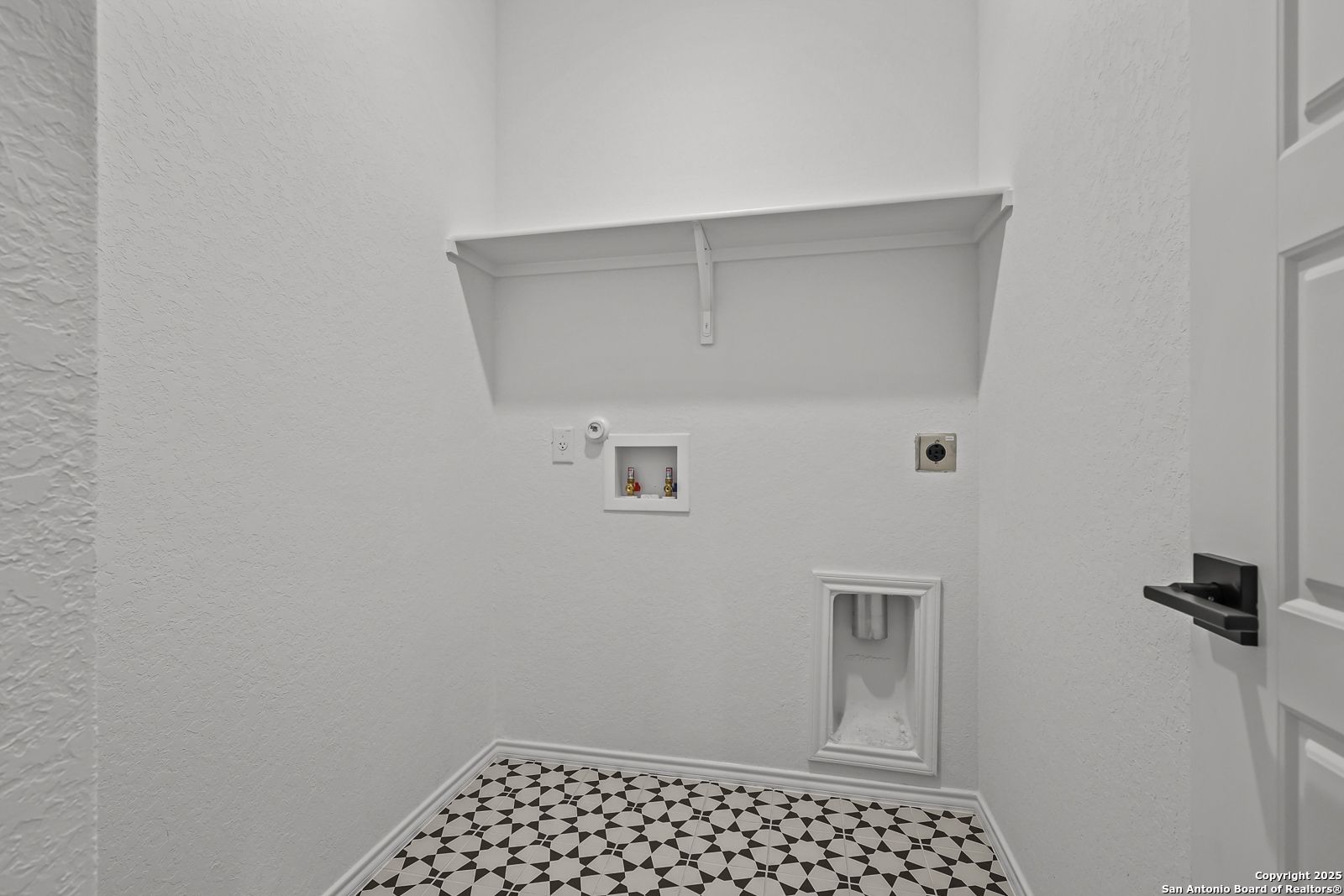 Modern white laundry room with utility sink, washer-dryer hookups, shelves, and geometric tile floor in The Daphne J, Converse, Texas