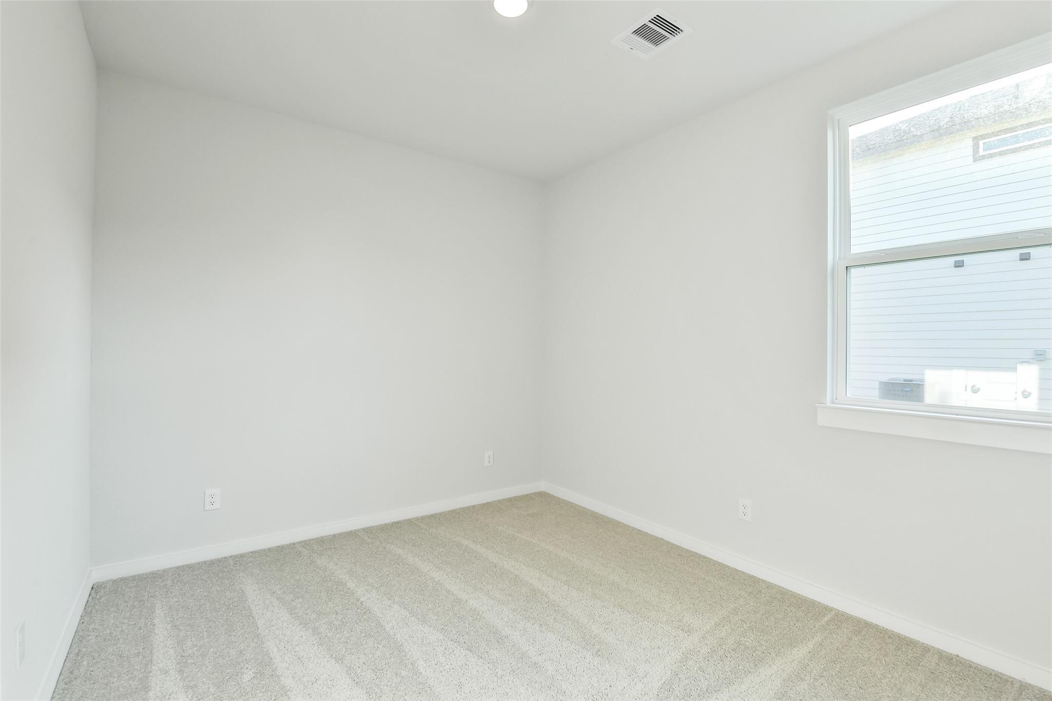 Empty secondary bedroom with beige carpet, white walls, and window in Davidson Homes The Colorado F, Cleveland Texas