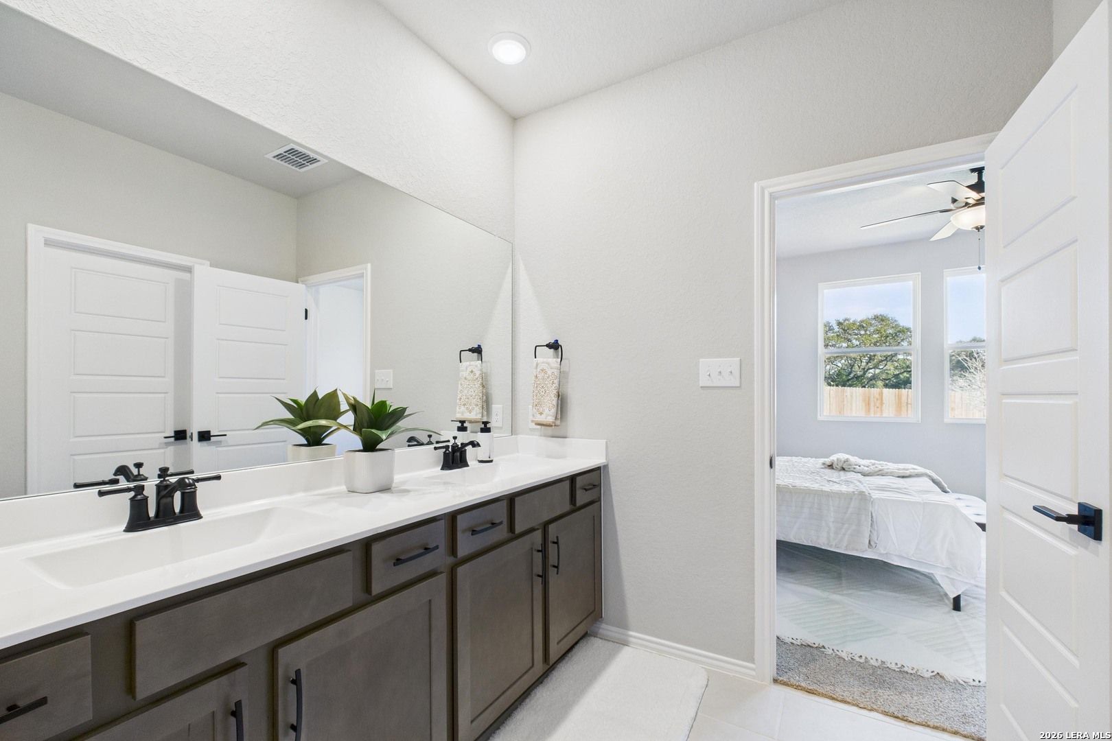 Modern master bathroom with double vanity, dark cabinets, and open door to bedroom in Davidson Homes The Douglas E, Bricewood, San Antonio