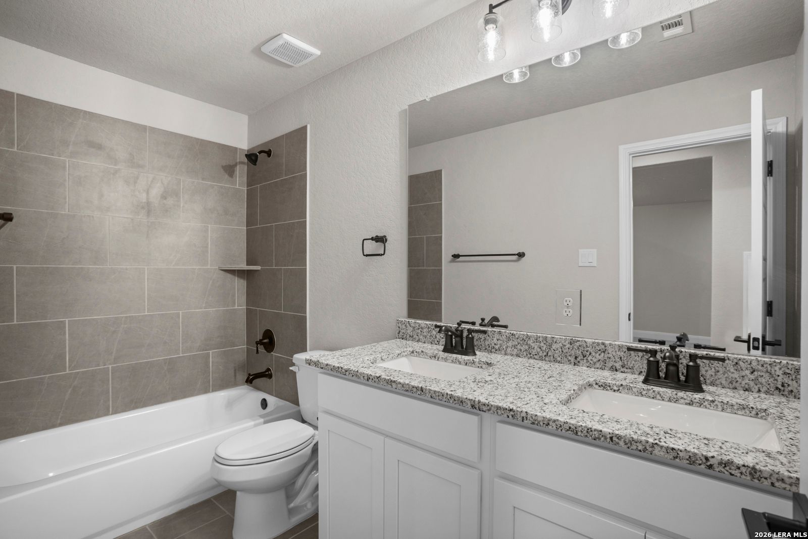 Modern bathroom with granite dual vanity, tiled shower-tub combo, and bronze fixtures in The Jennings G plan, Ladera.