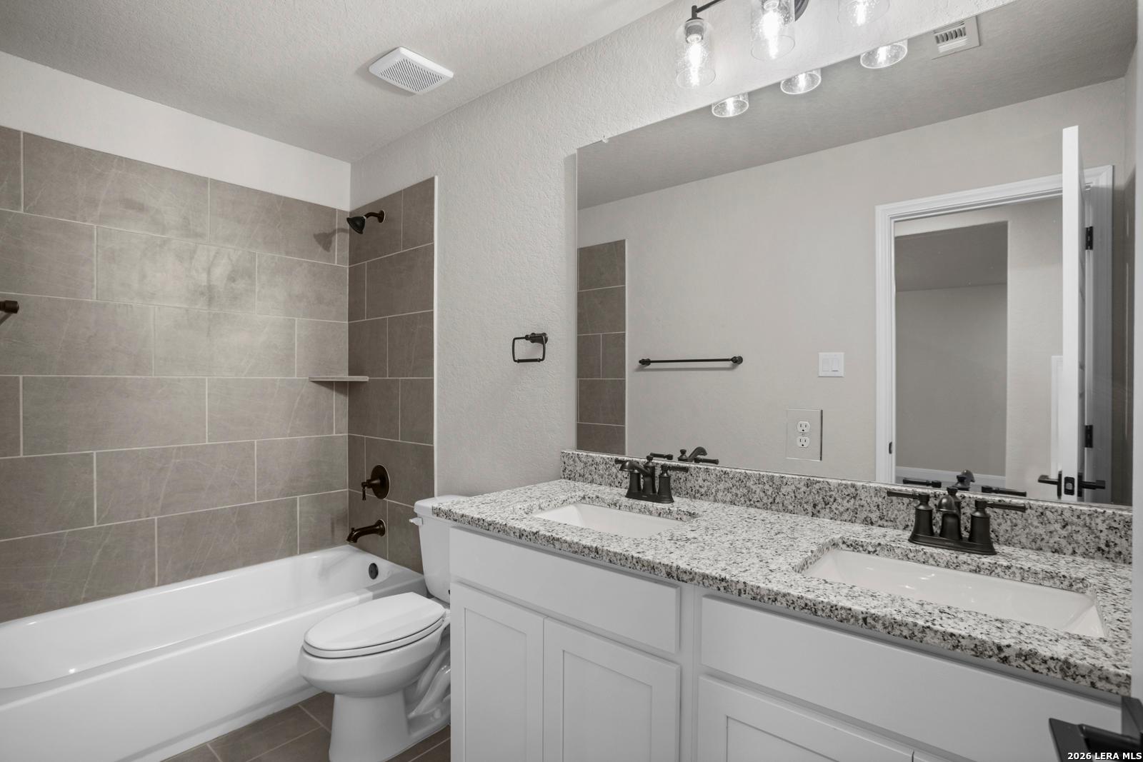 Modern bathroom with granite dual vanity, tiled shower-tub combo, and bronze fixtures in The Jennings G plan, Ladera.