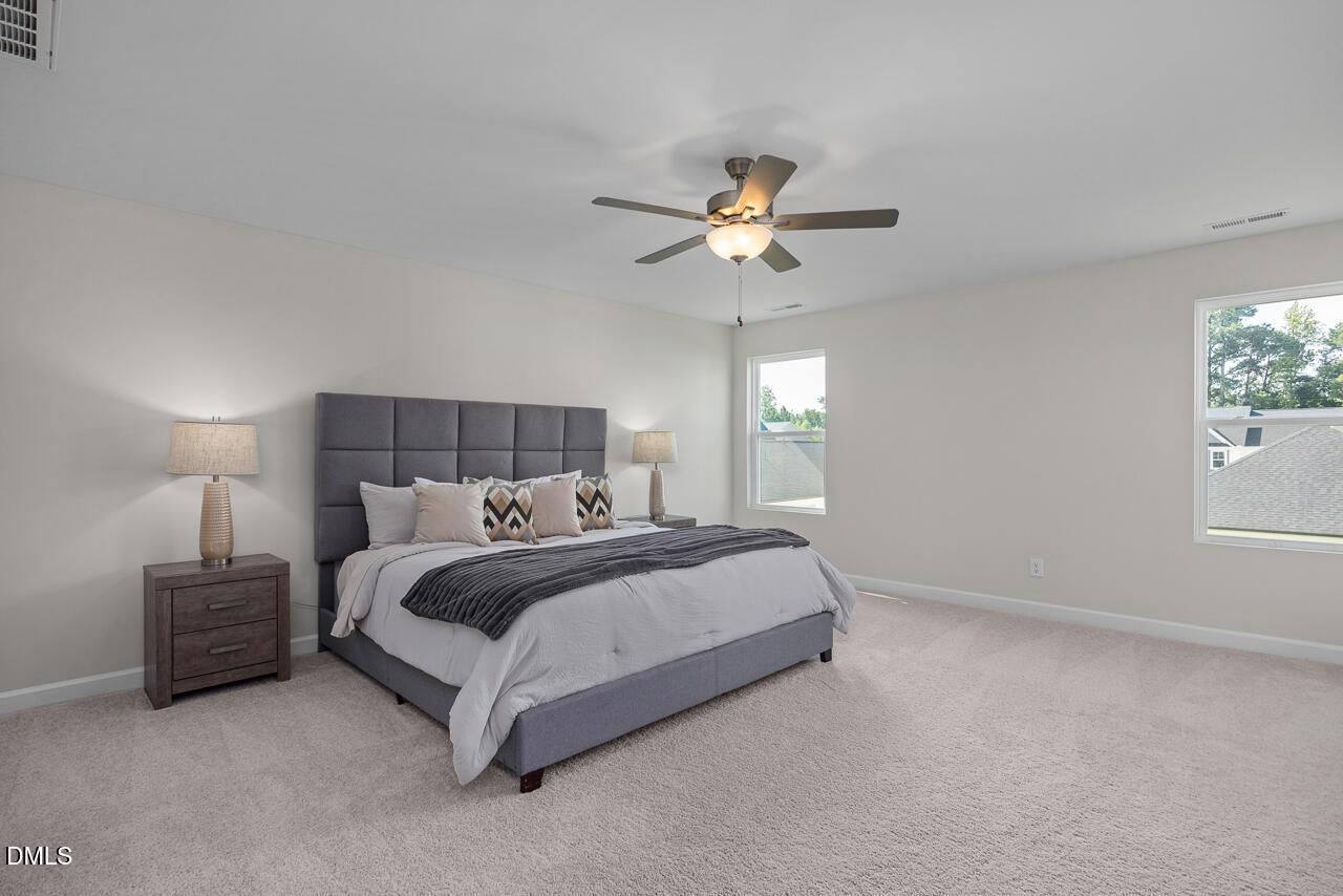 Elegant master bedroom with king bed, gray headboard, ceiling fan, and large windows in Davidson Homes The Preston A, Lillington, NC